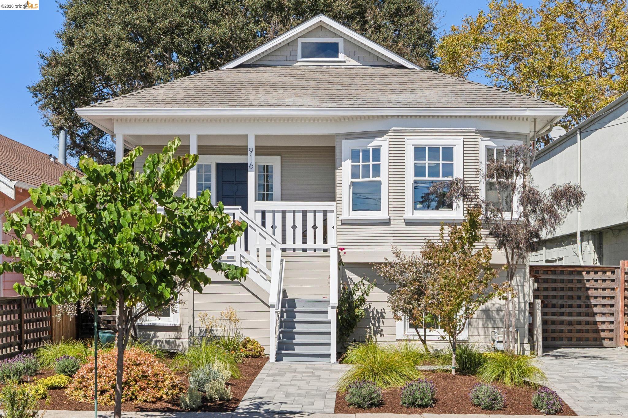 Light gray house with a covered porch, bay windows, and landscaped front garden.
