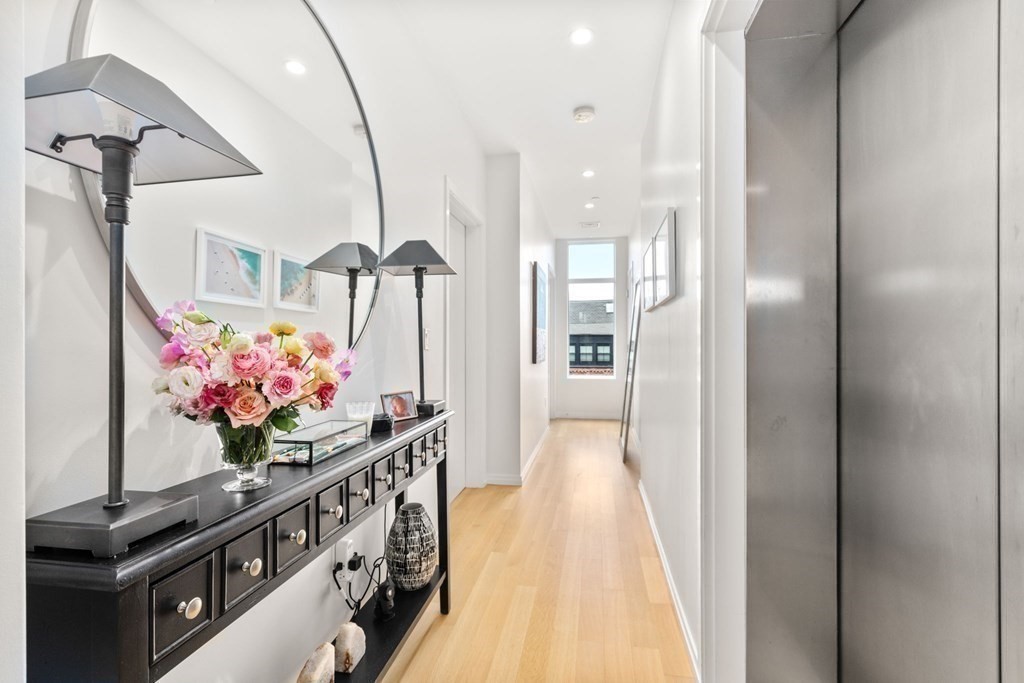 Apartment hallway with a flower-topped black console, round mirror, and stainless-steel elevator doors.