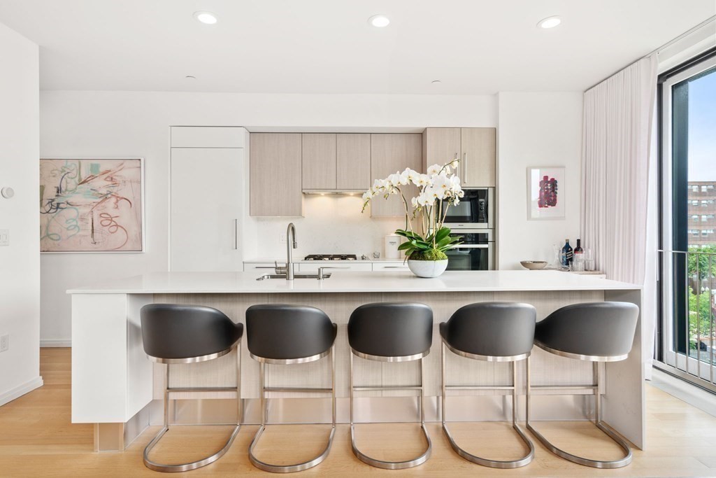 Modern kitchen with a large island, five bar stools, pale wood cabinetry, and orchids.