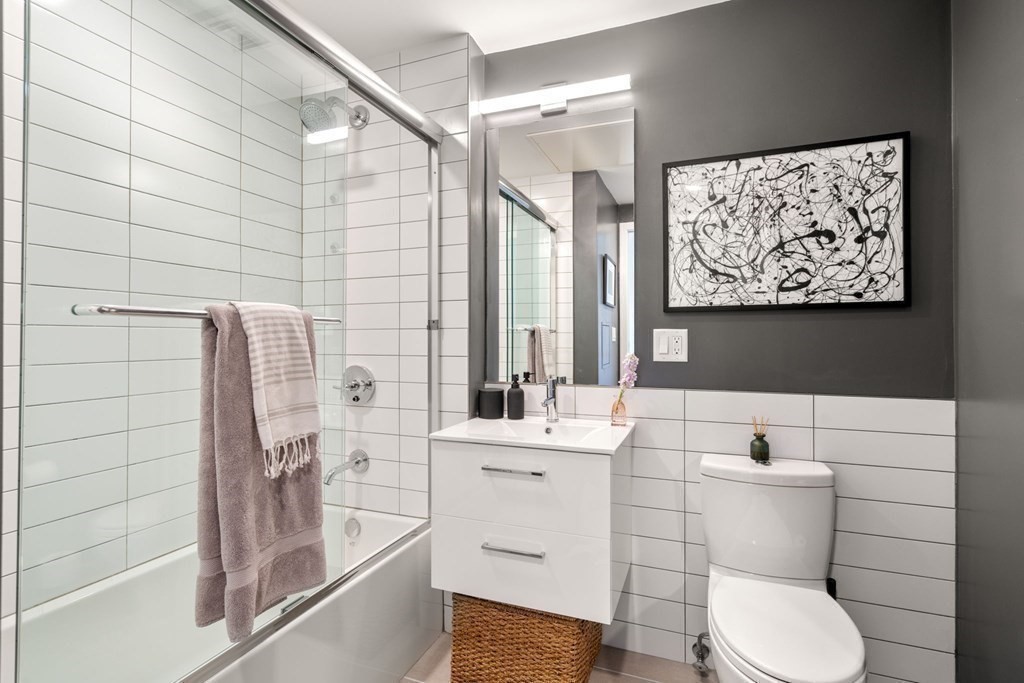 Bathroom with glass-enclosed tub, white tile, floating vanity, and framed abstract artwork.