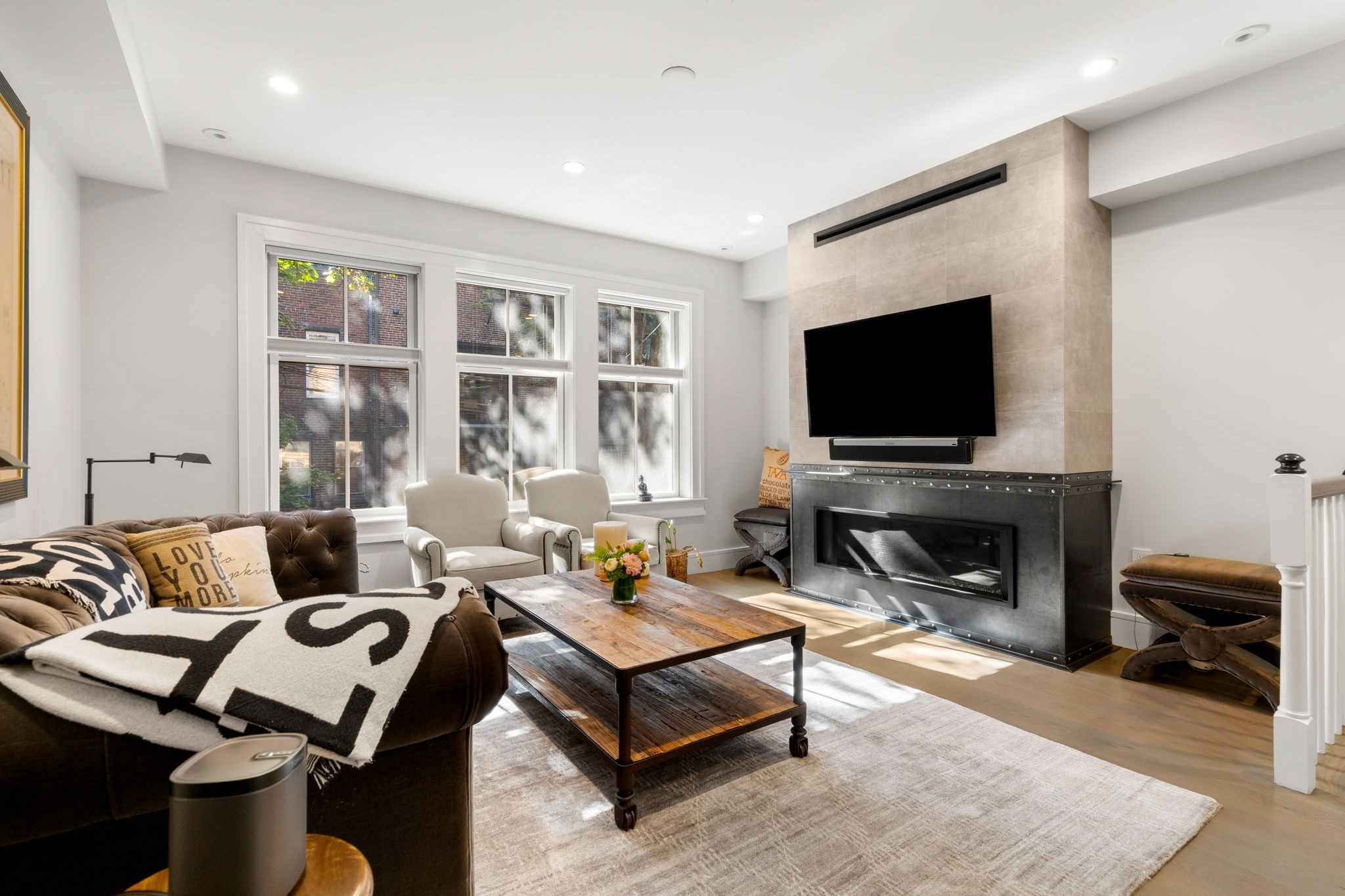 Living room with a tiled fireplace, mounted TV, tufted sofa, and three sunlit windows.