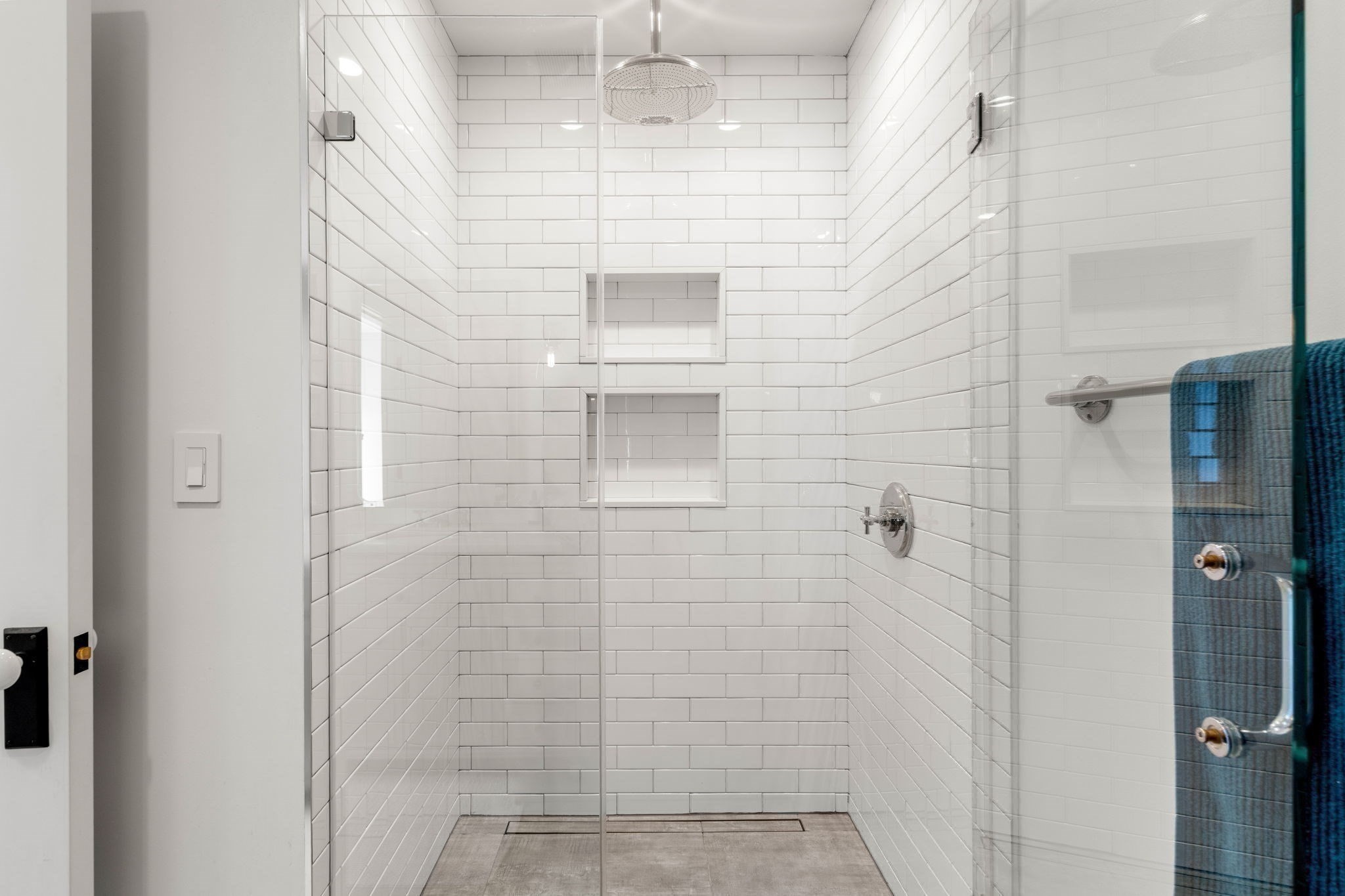 Walk-in shower with white subway tile, two recessed niches, and a large rainfall showerhead.
