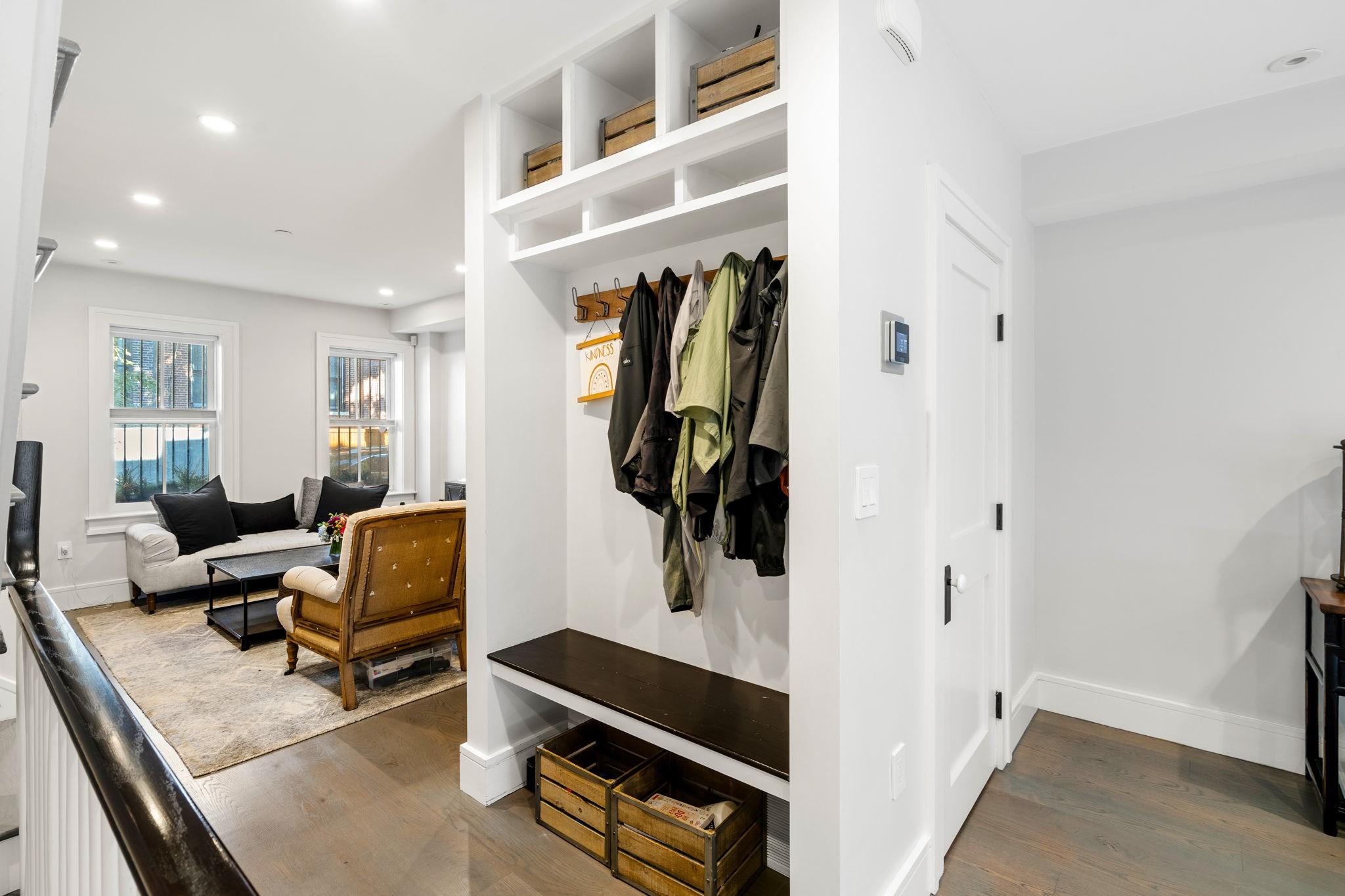 Built-in entryway with coat hooks, jackets, storage cubbies, and a dark wood bench beside the living room.