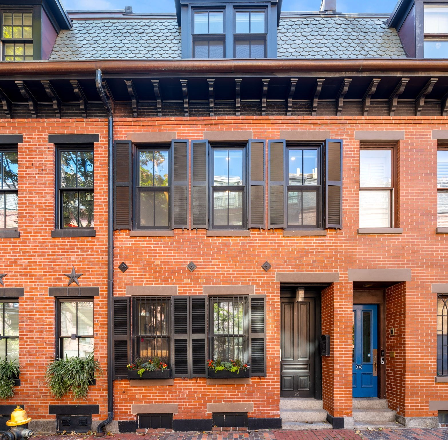 Red-brick townhouse facade with dark shutters, flower boxes, and two recessed entry doors.