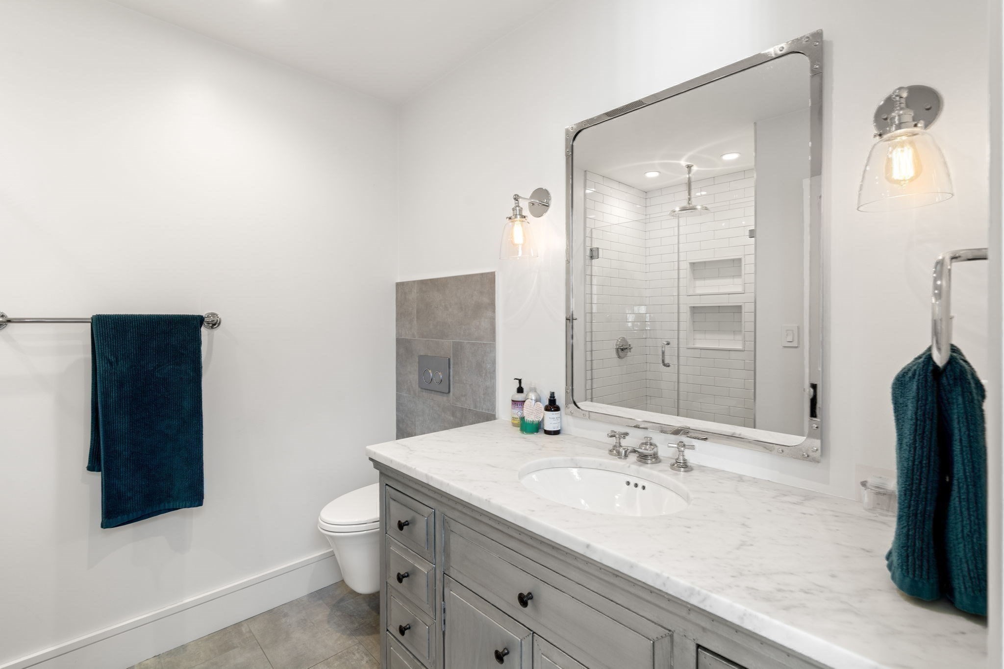Bathroom with a gray vanity, marble countertop, and subway-tile shower with built-in niches.