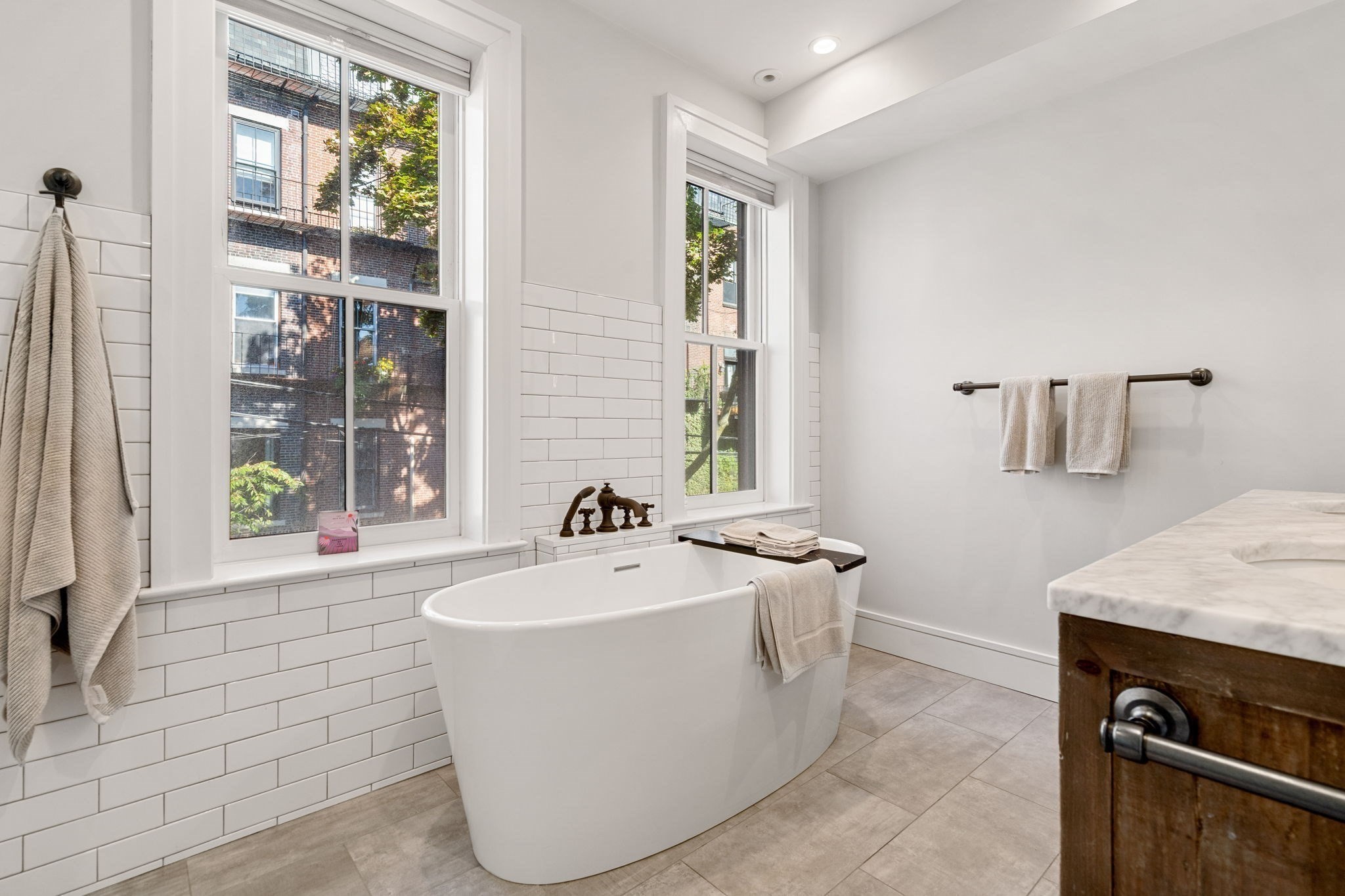 Bathroom with a freestanding tub beneath tall windows and white subway tile.