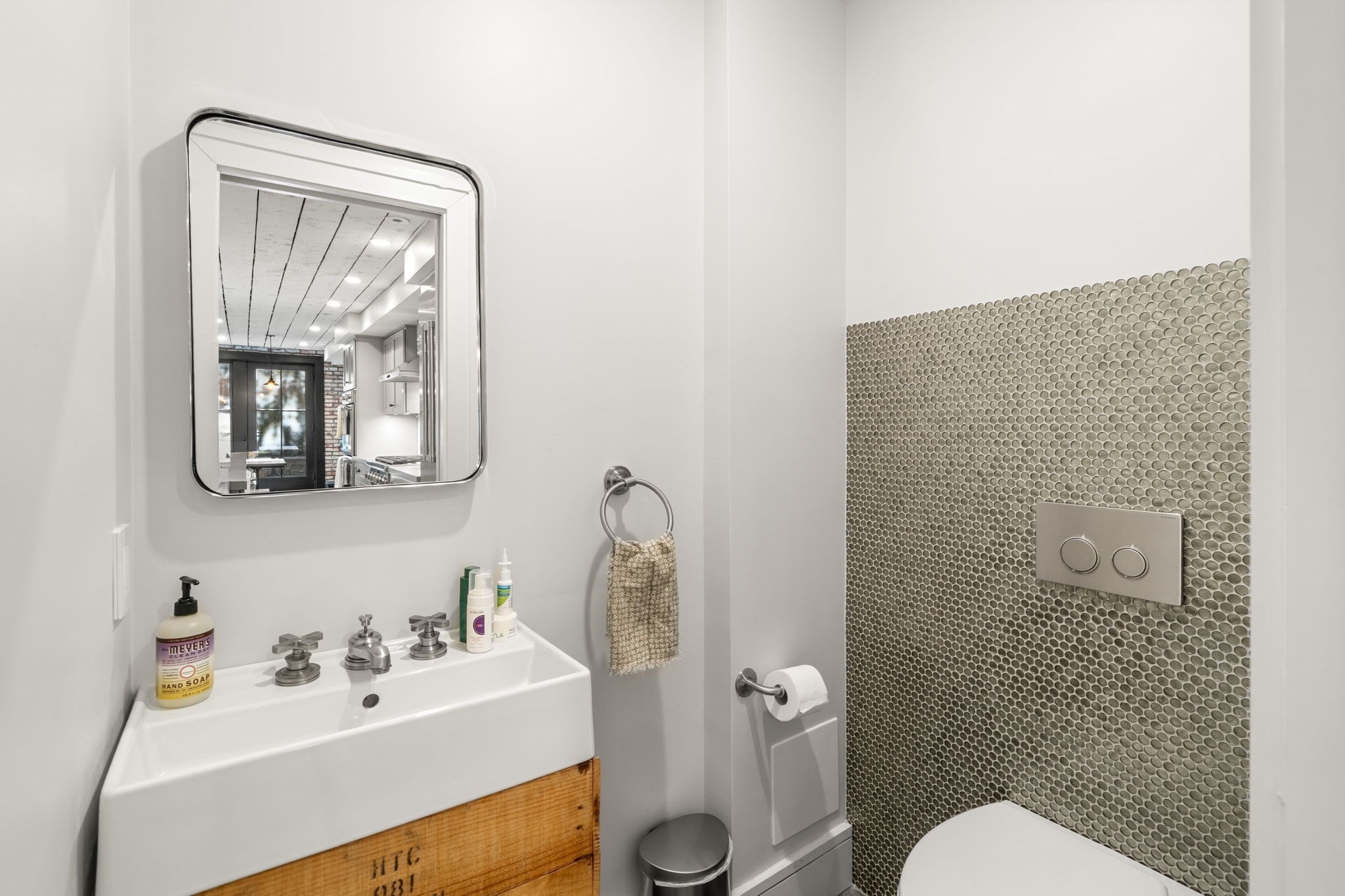Modern bathroom with a wood-front sink vanity, chrome-framed mirror, and gray circular mosaic tile wall.