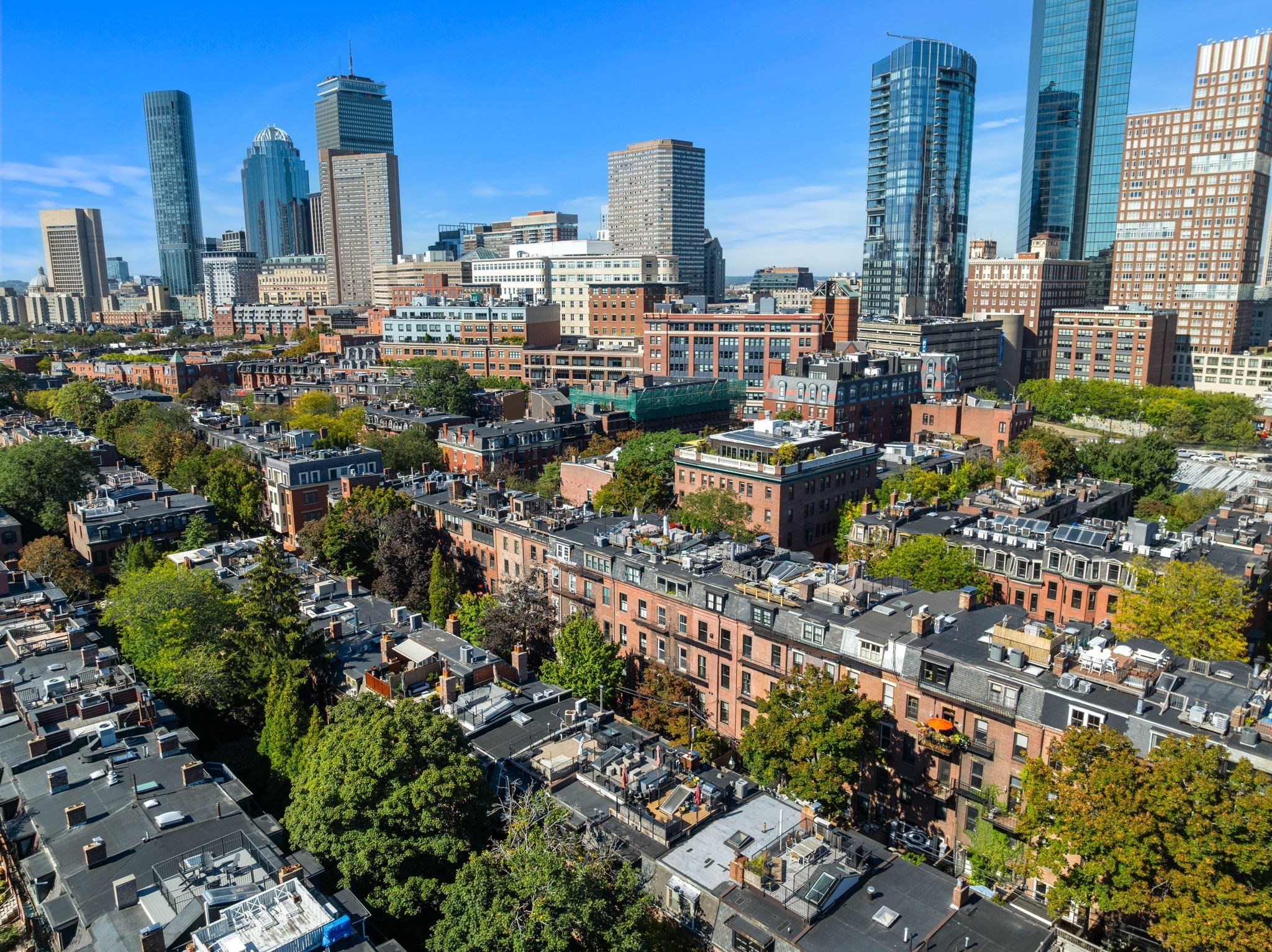 Aerial Boston view over tree-lined rooftops toward the downtown skyline.