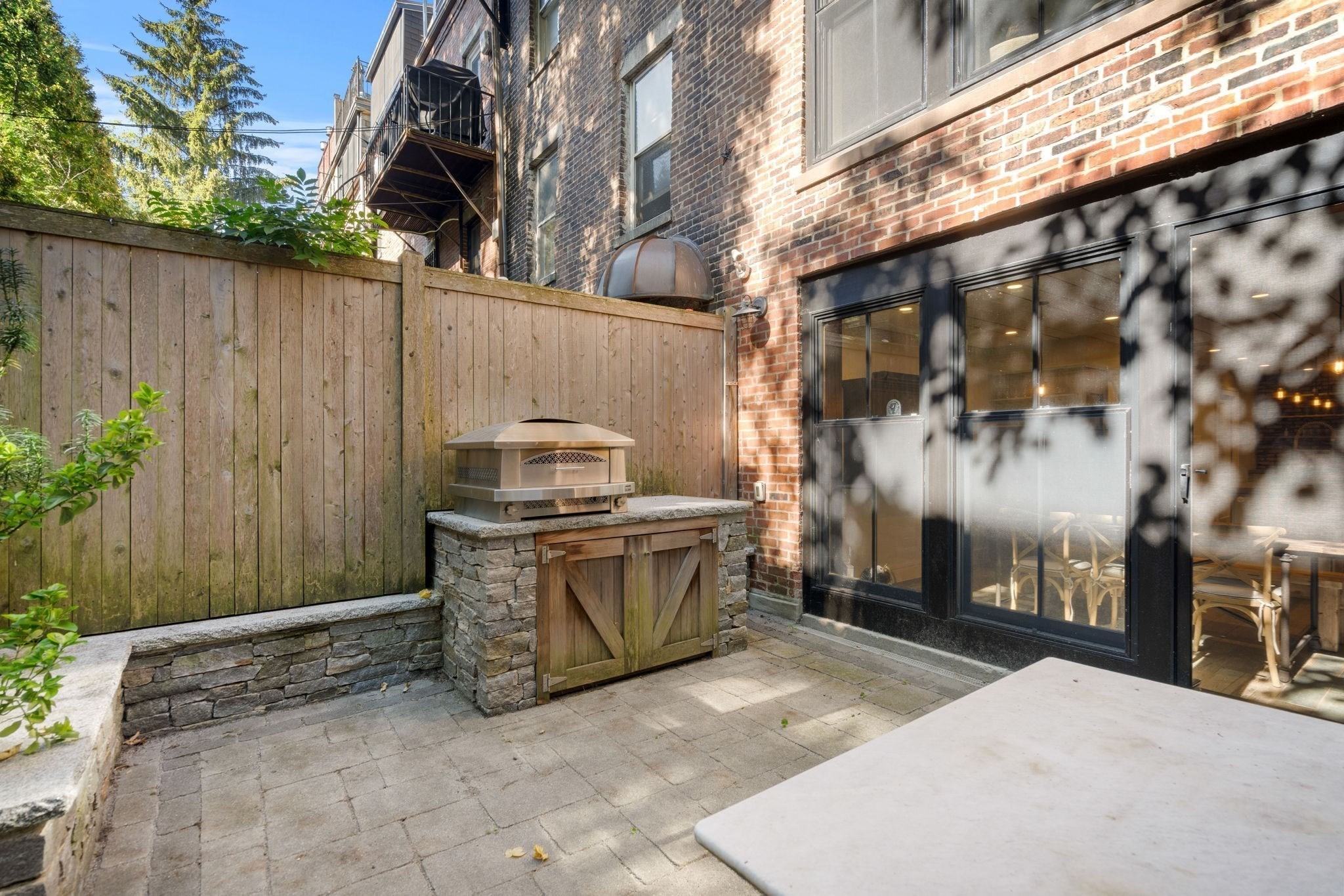Brick-walled patio with a built-in grill, wooden privacy fence, and black-framed glass doors.