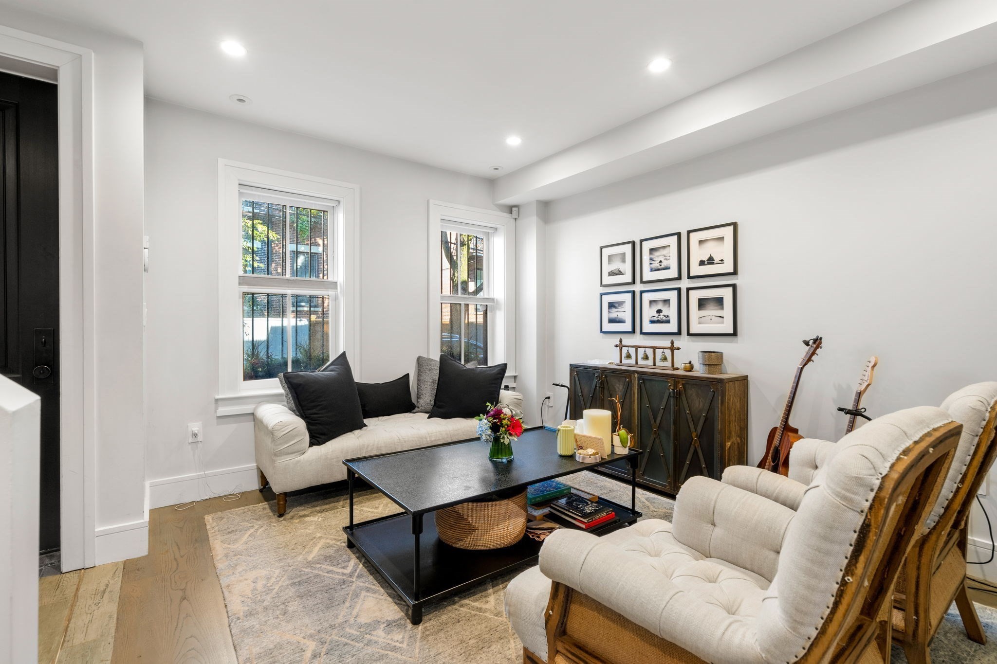 Living room with cream sofas, a black coffee table, framed prints, and two guitars.