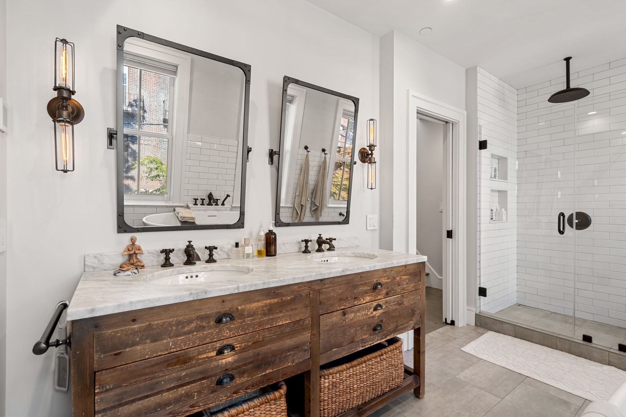 Bathroom with a rustic double vanity, marble countertop, framed mirrors, and a glass-enclosed subway-tile shower.