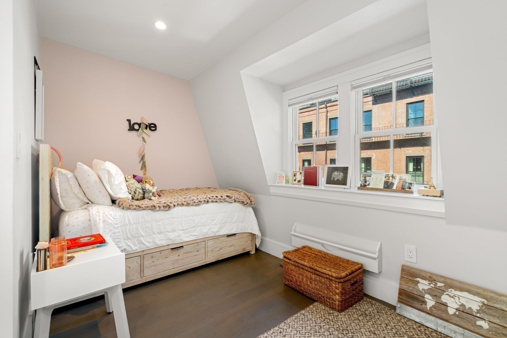Bedroom with a wood storage bed, sloped ceiling, and large windows overlooking a brick building.