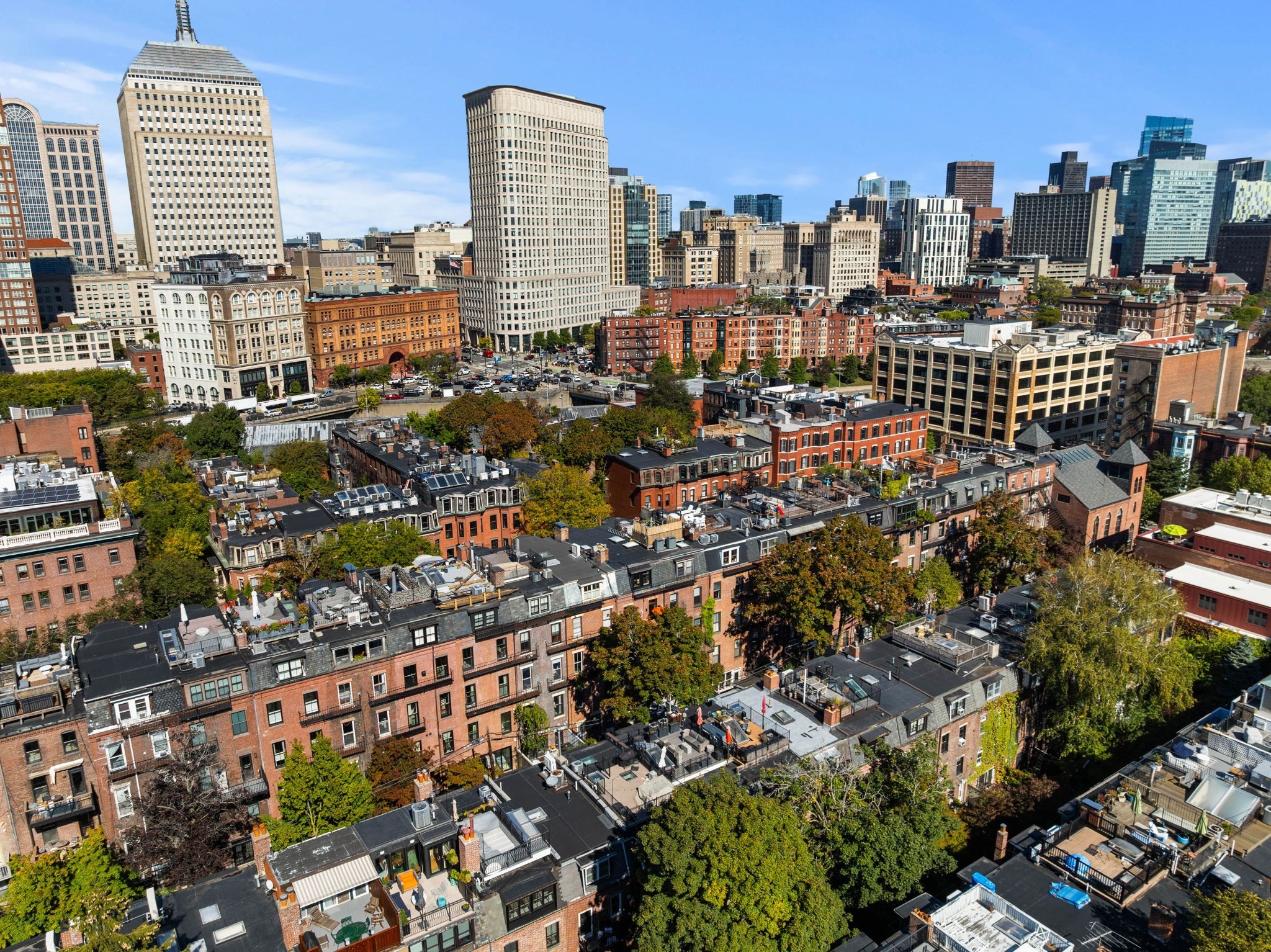 Aerial view of Boston rooftops and brick row houses with the downtown skyline beyond.
