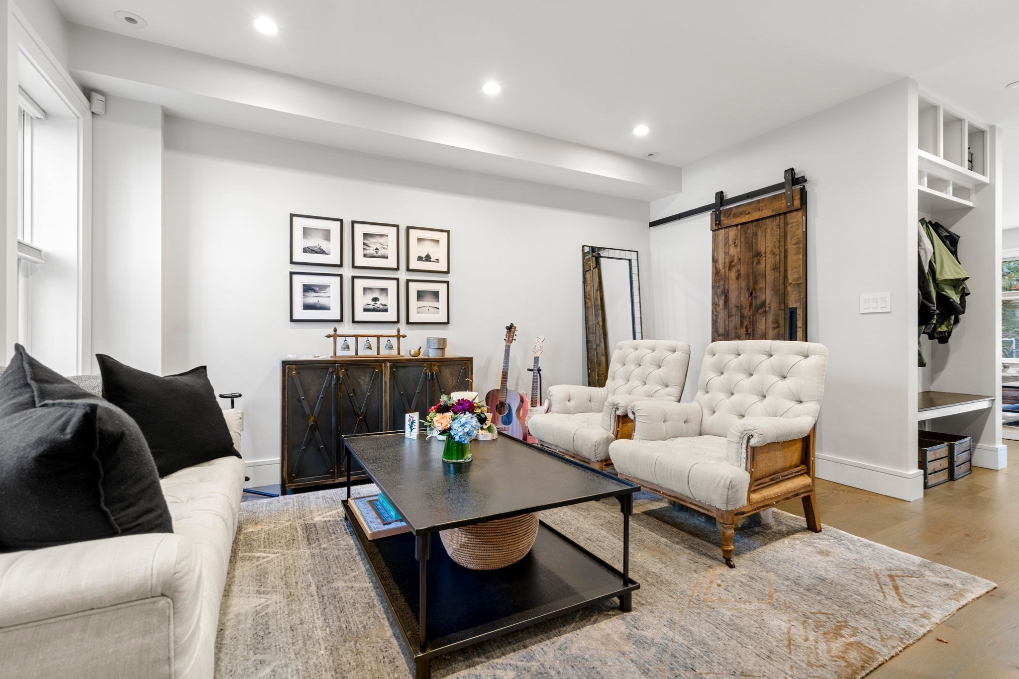 Furnished living room with tufted white chairs, a black coffee table, and a rustic sliding barn door.