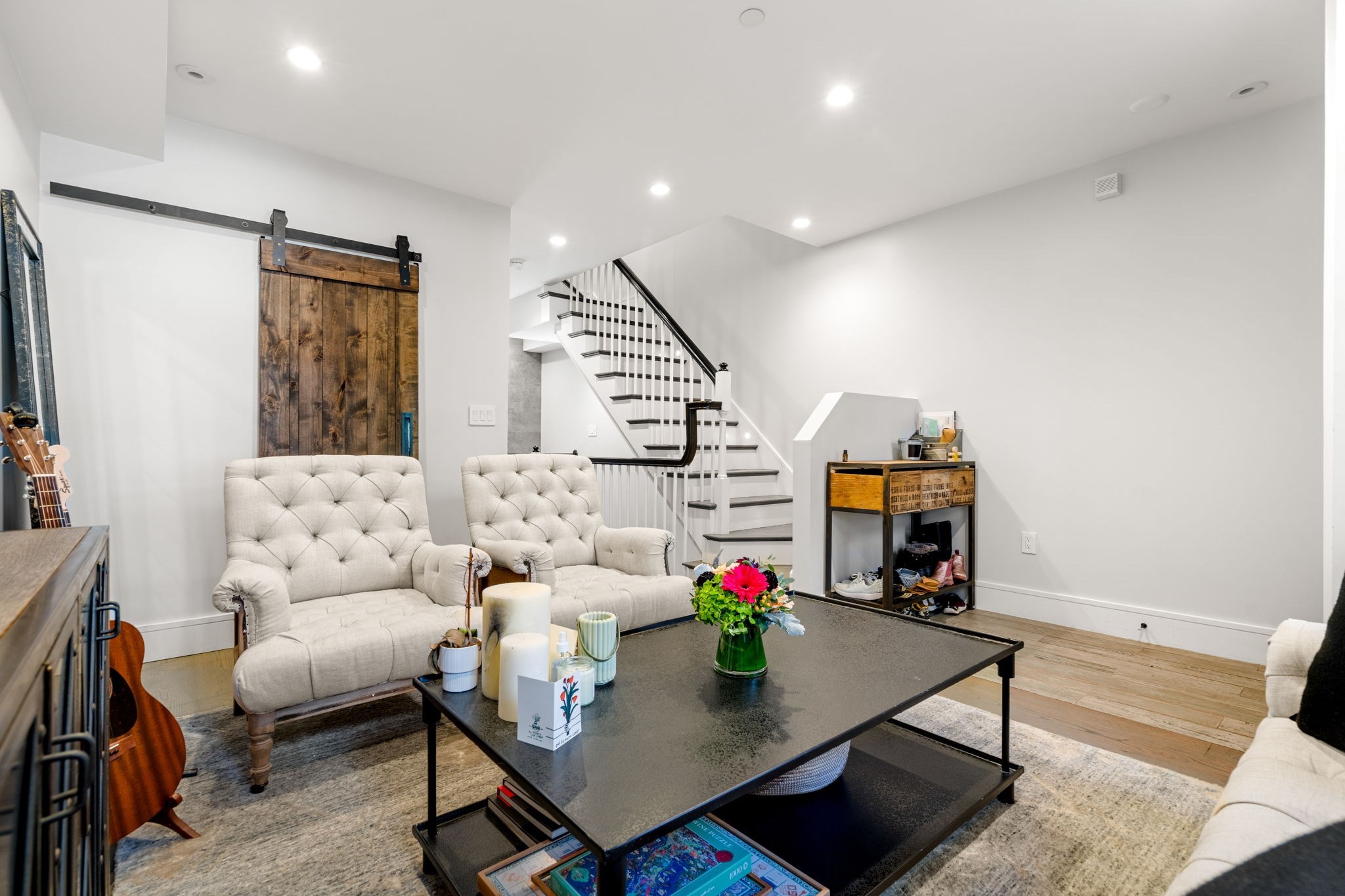 Living room with tufted cream sofas, a rustic sliding barn door, and an open staircase.