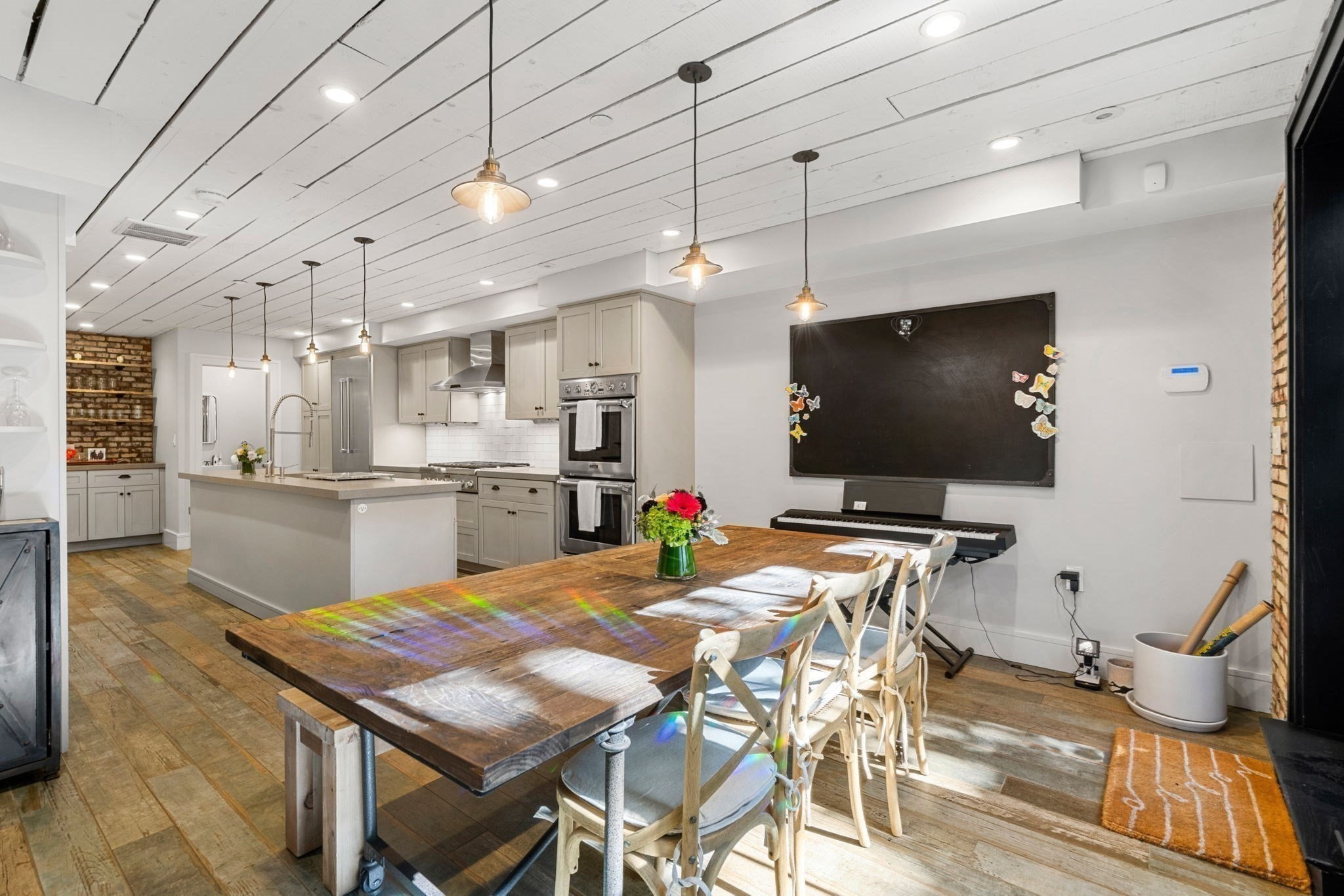 Open-plan kitchen and dining area with a large rustic wood table, gray cabinetry, and stainless steel appliances.