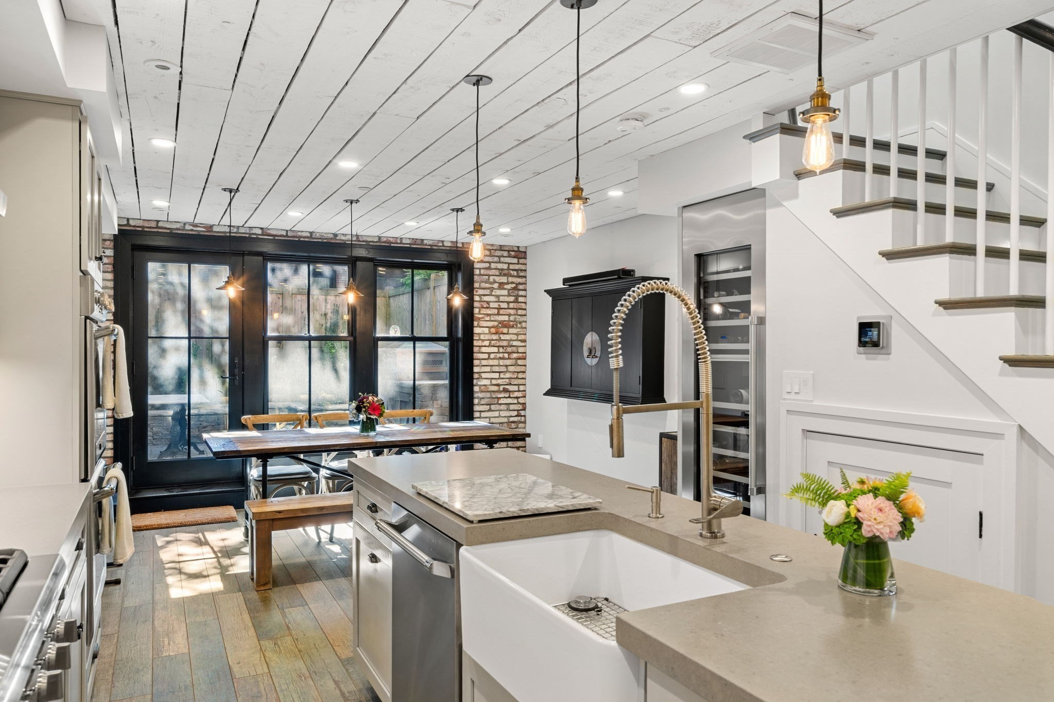 Kitchen with a large island, farmhouse sink, and dining area beside black-framed glass doors.