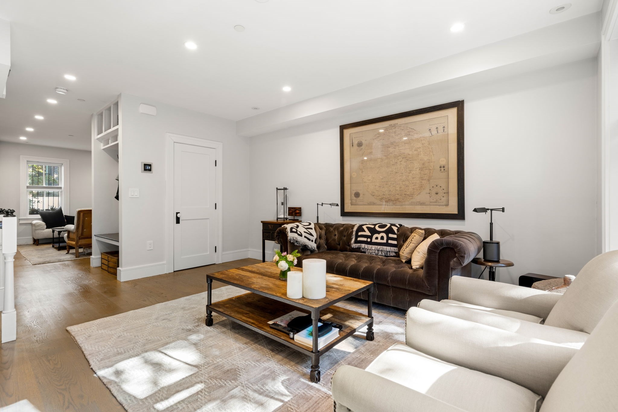 Living room with a tufted brown sofa, cream armchairs, and a large framed map.