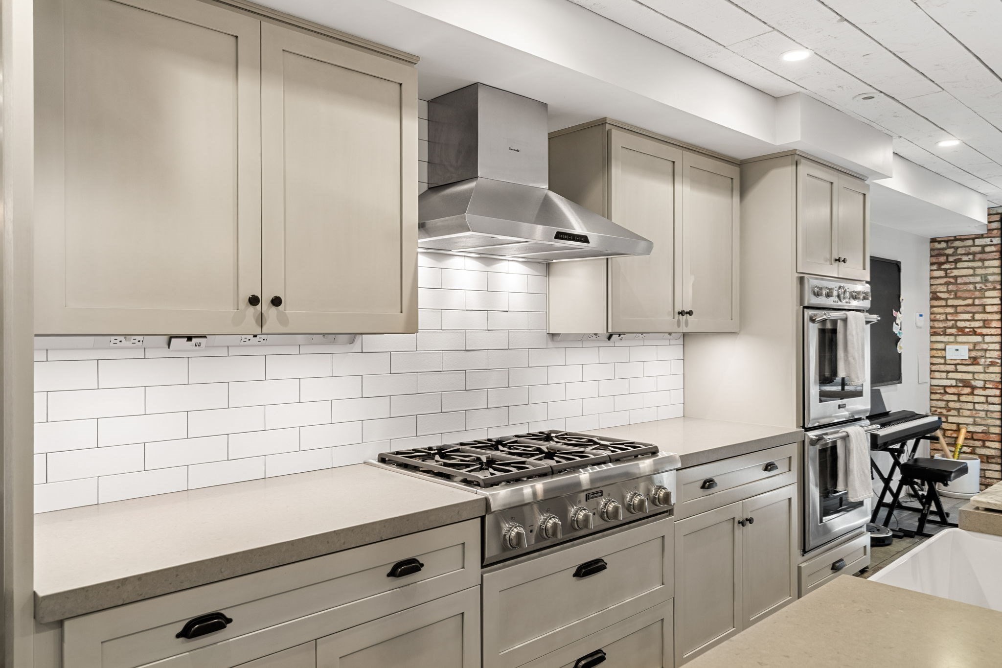Kitchen with cream cabinets, subway tile backsplash, stainless steel range, and stacked wall ovens.