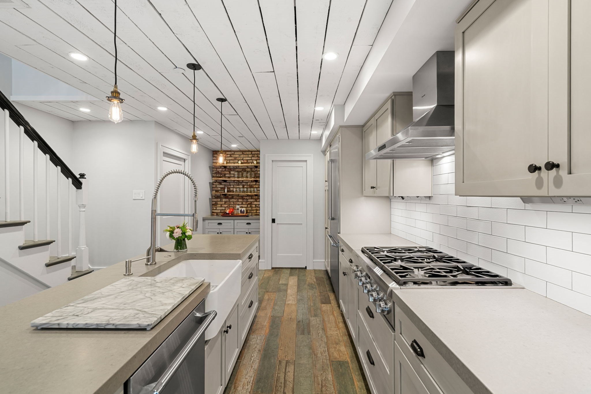 Renovated galley kitchen with a farmhouse sink, stainless steel range, and brick-backed shelving nook.