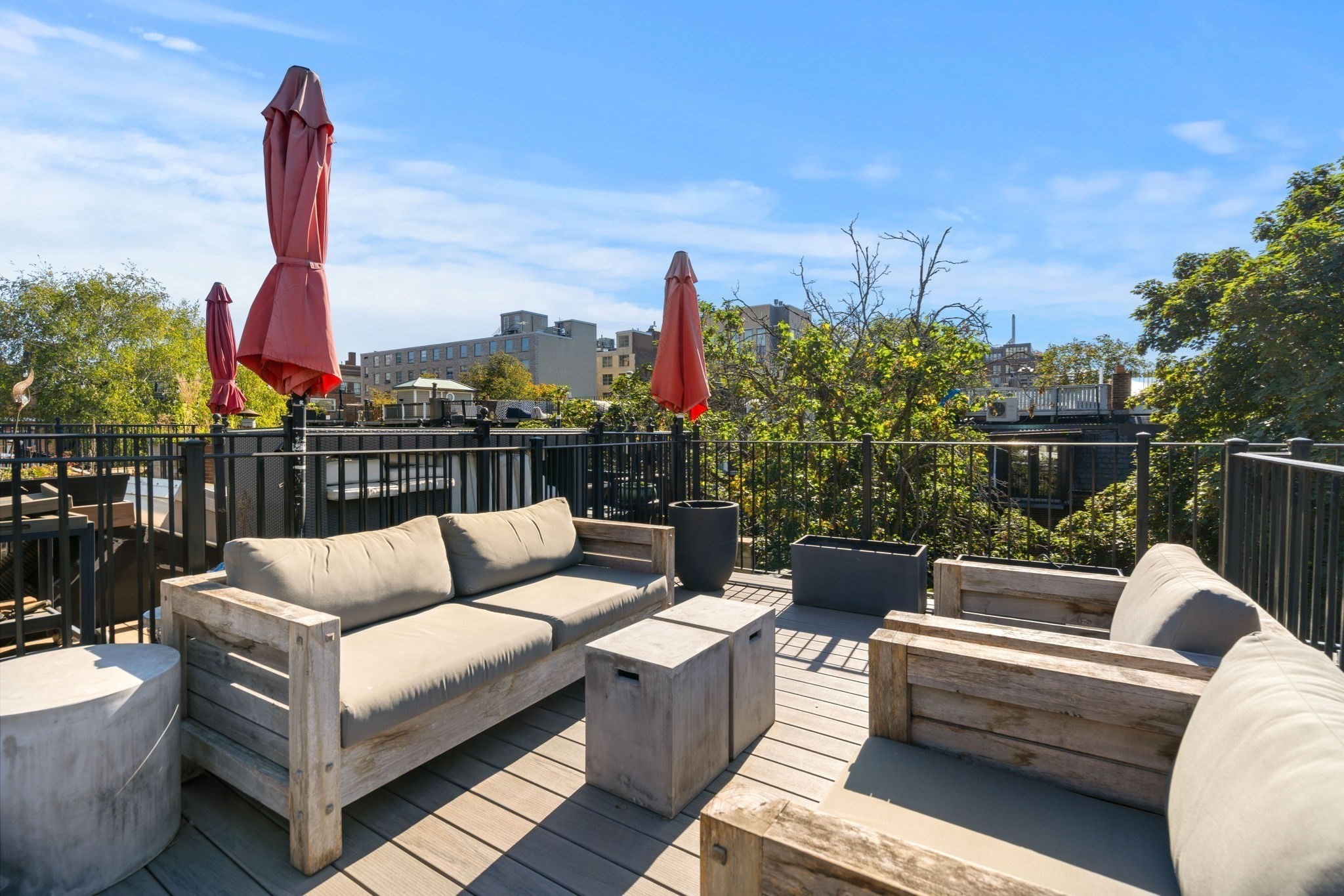 Rooftop deck with wood lounge seating, red umbrellas, and views of nearby city buildings.