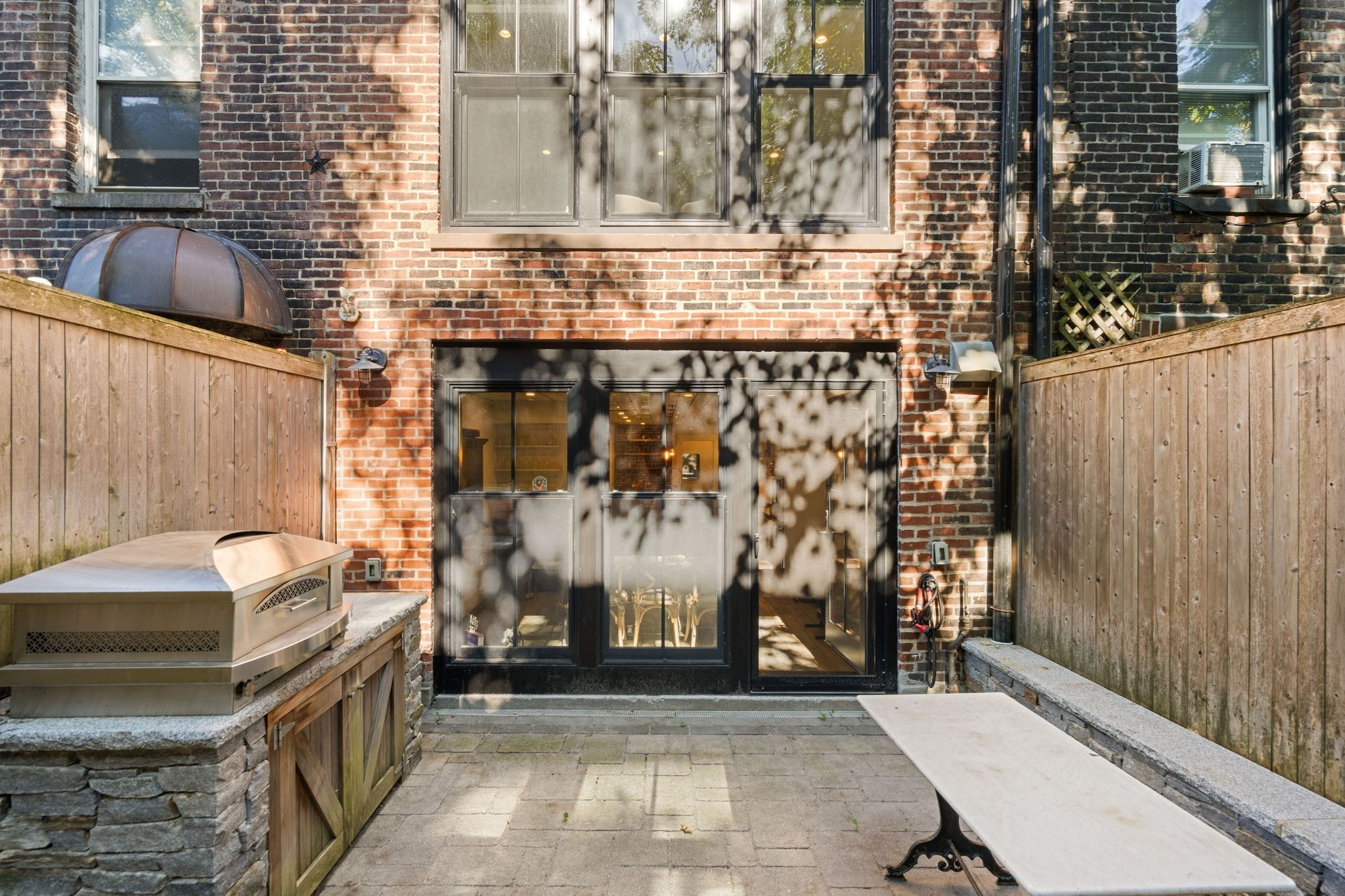 Private brick-walled patio with a grill, wooden privacy fences, and black-framed glass doors.