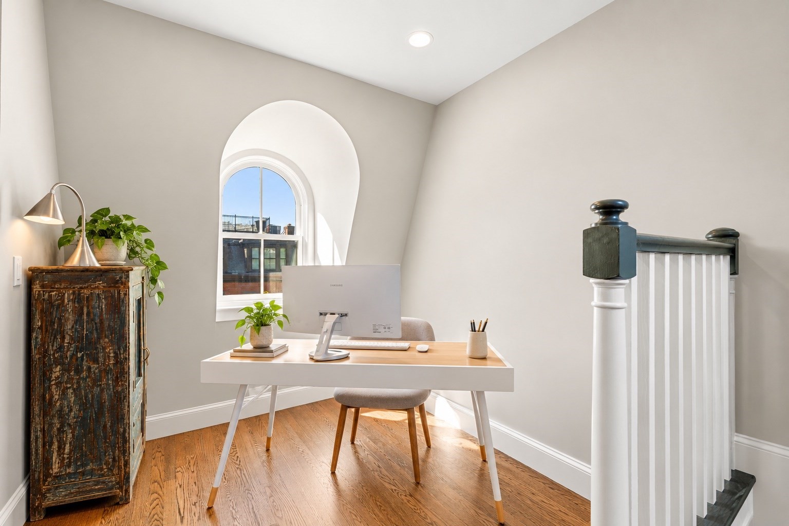 Home office with an arched window, desk, computer, and hardwood floors.