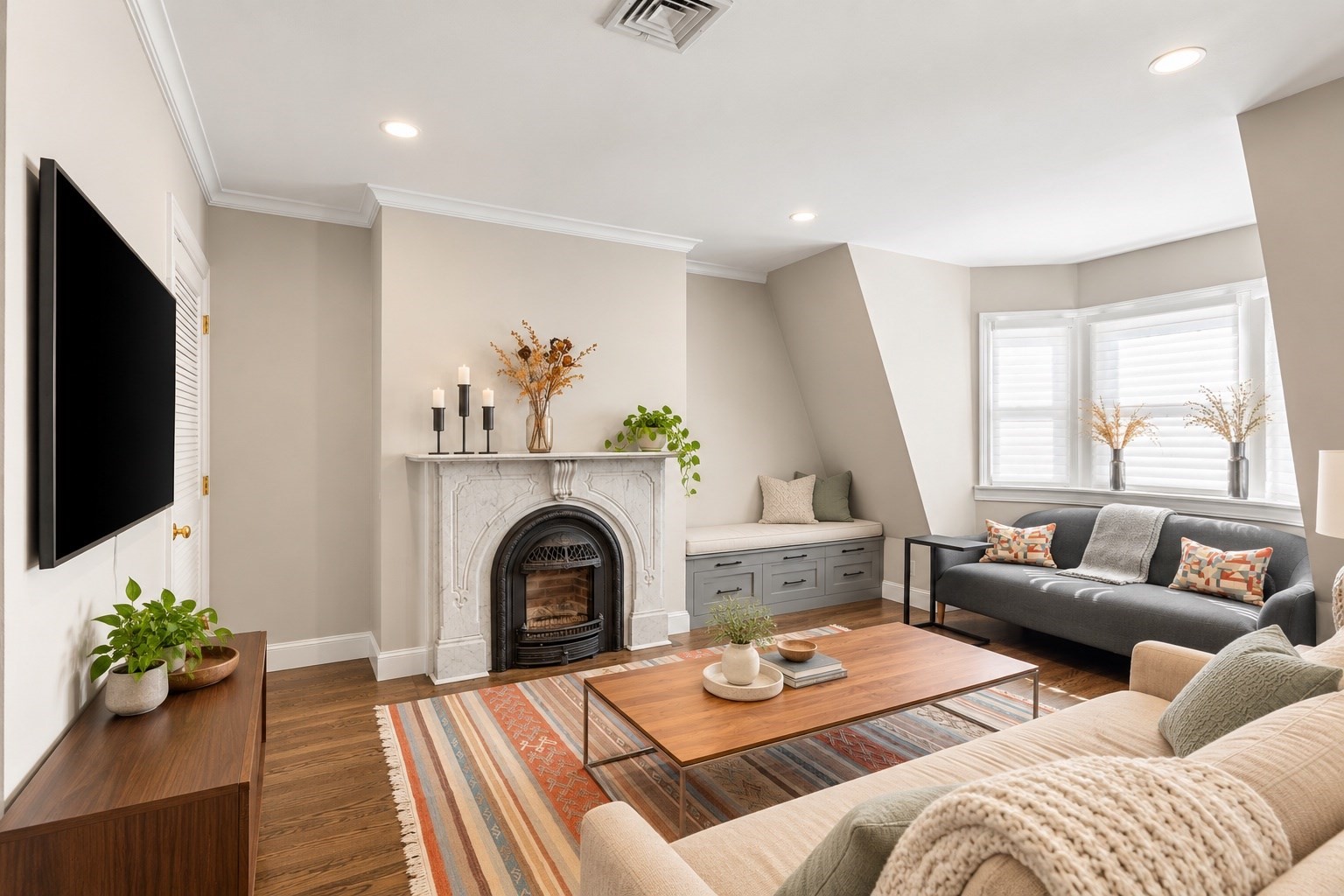 Staged living room with a marble fireplace, built-in window seat, and gray sofa.