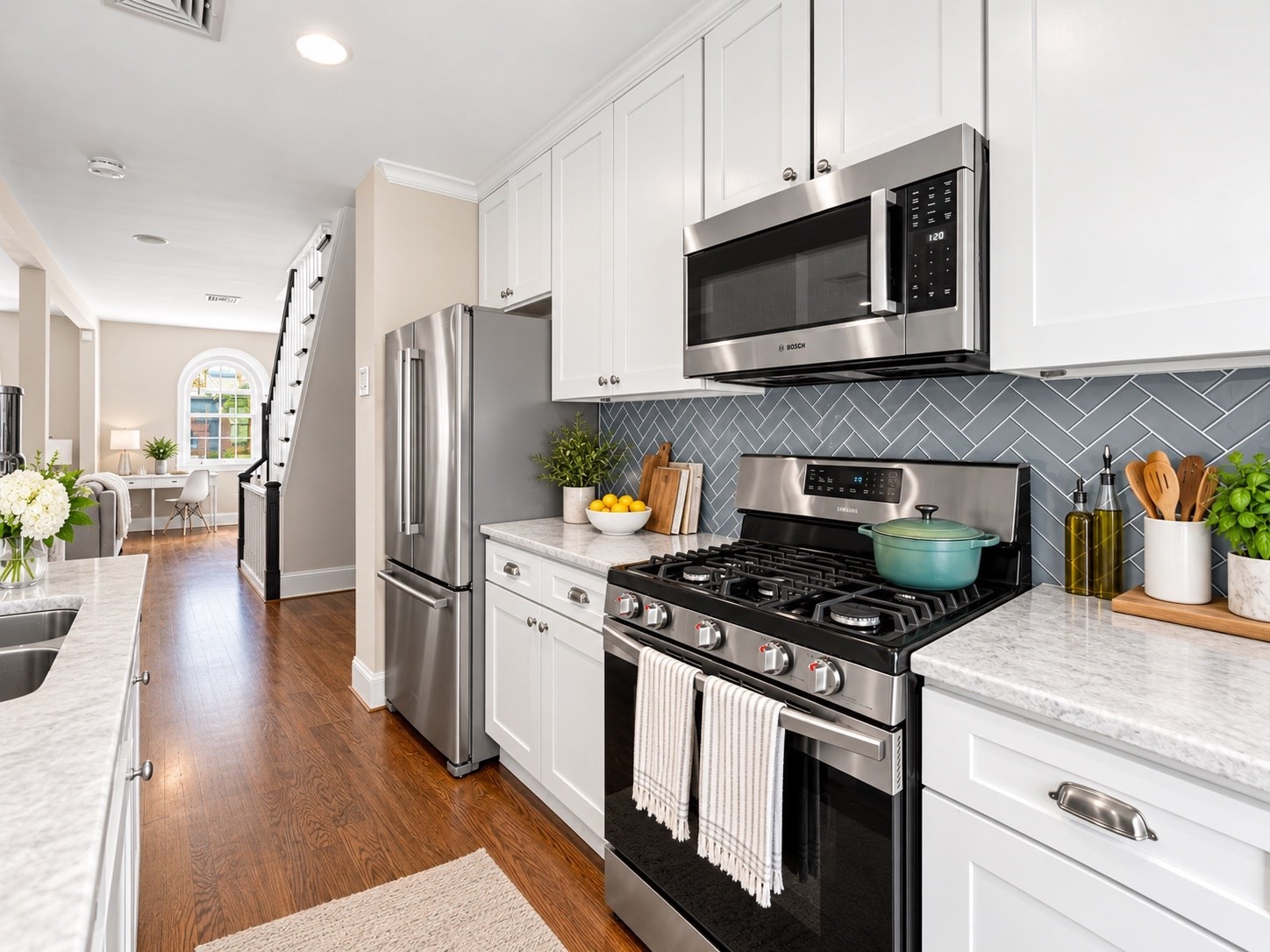 Kitchen with white cabinets, herringbone backsplash, stainless appliances, and a prominent gas range.