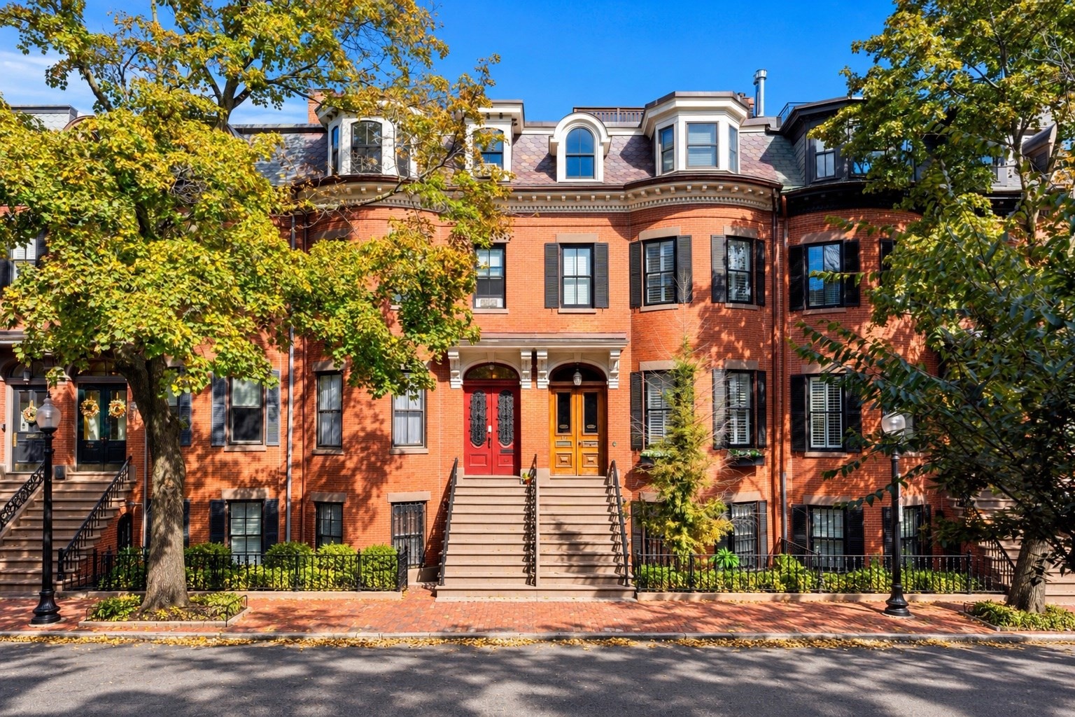 Red-brick townhouses with ornate dormers and raised stoops, framed by autumn trees.