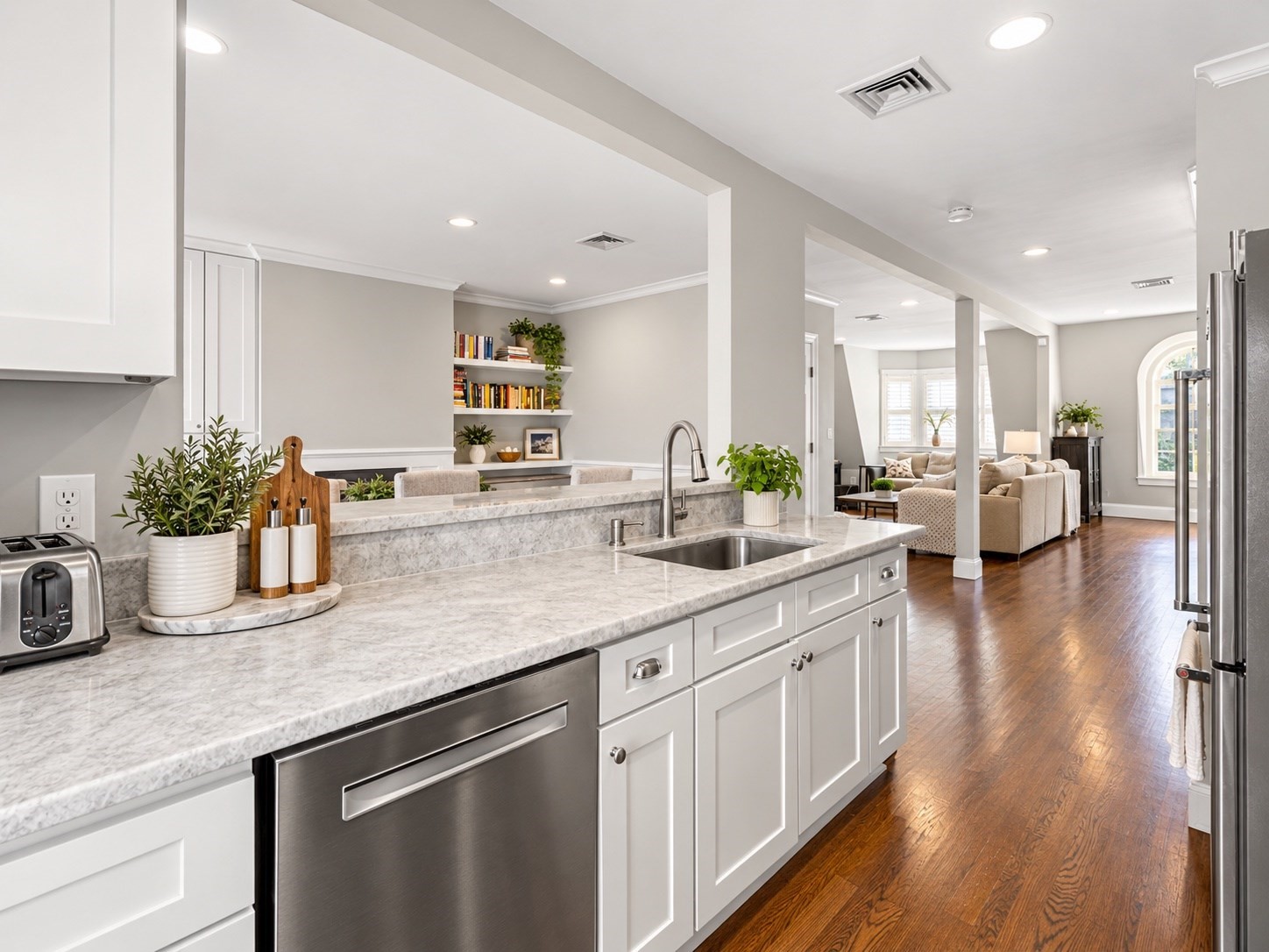 Open-plan kitchen with marble counters, white cabinets, and hardwood floors leading to the living room.