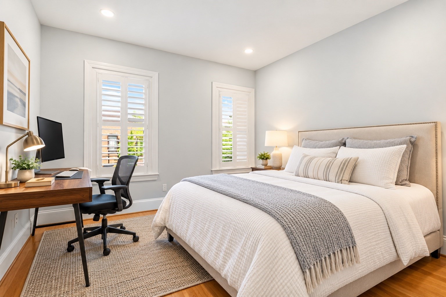 Bright bedroom with a large white bed, shuttered windows, and a wooden desk.