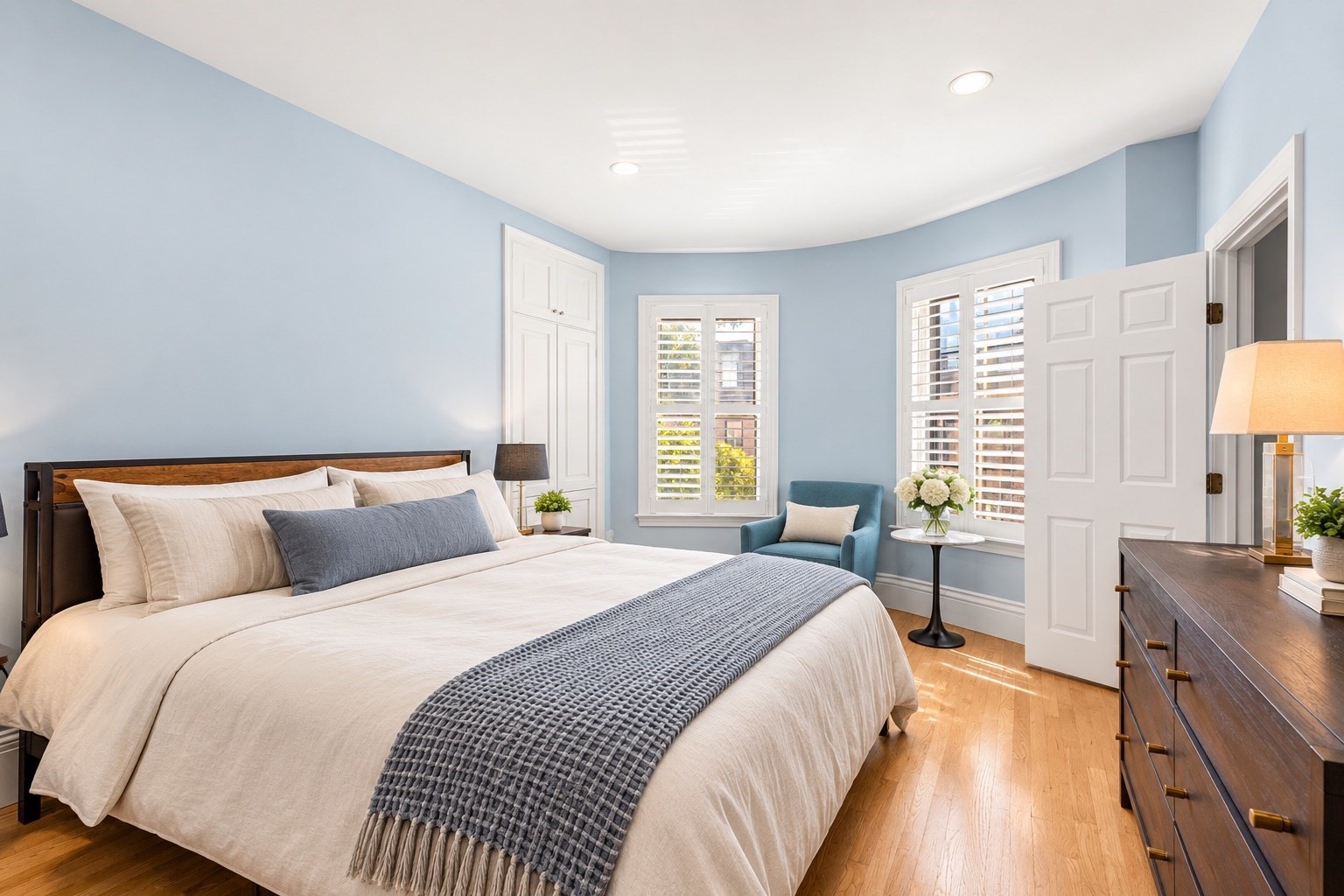 Bedroom with a large bed, blue walls, plantation shutters, and hardwood floors.