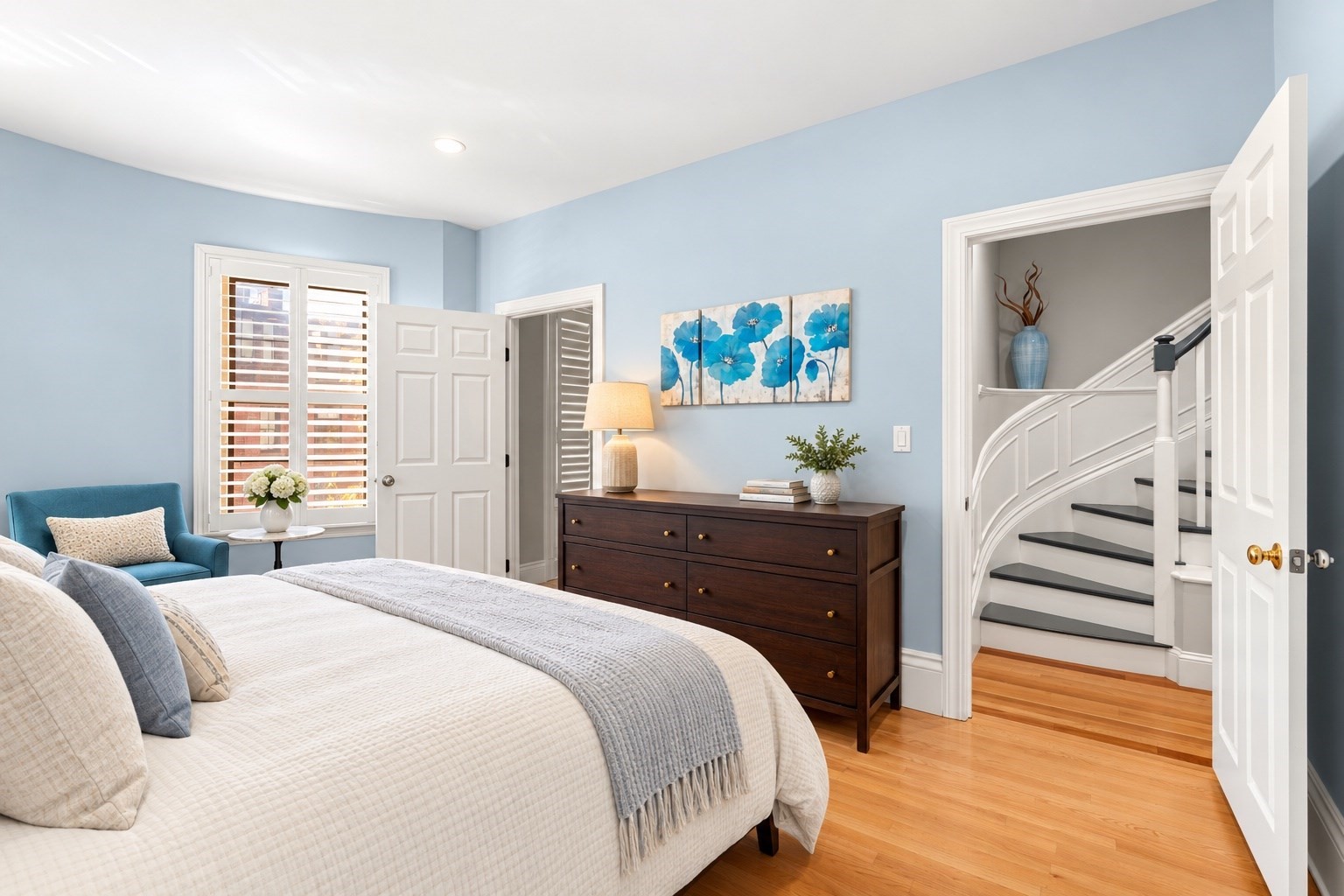 Staged bedroom with a white bed, blue walls, and an open doorway to a curved staircase.