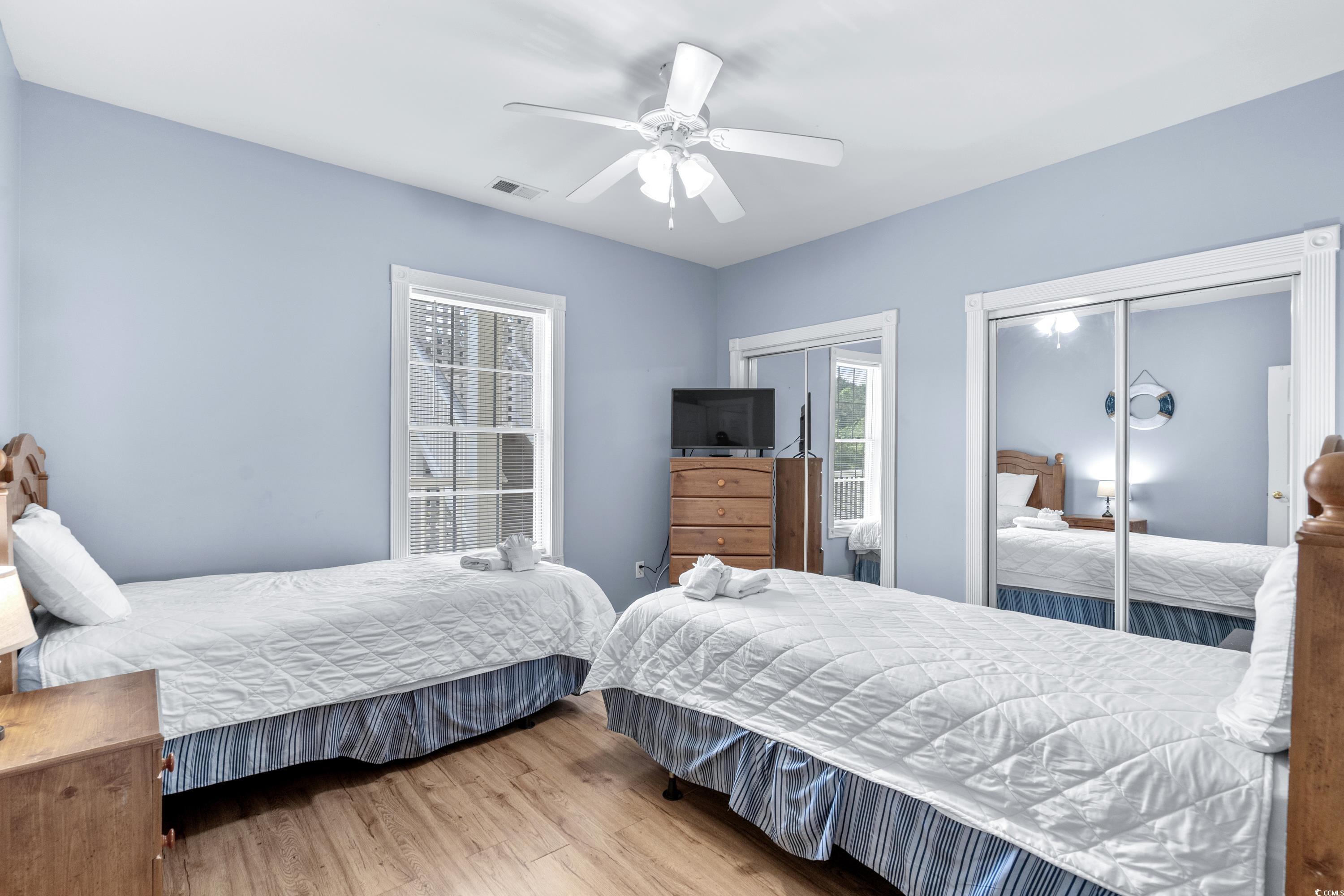 Bedroom with two white-quilted beds, a ceiling fan, and mirrored closet doors.