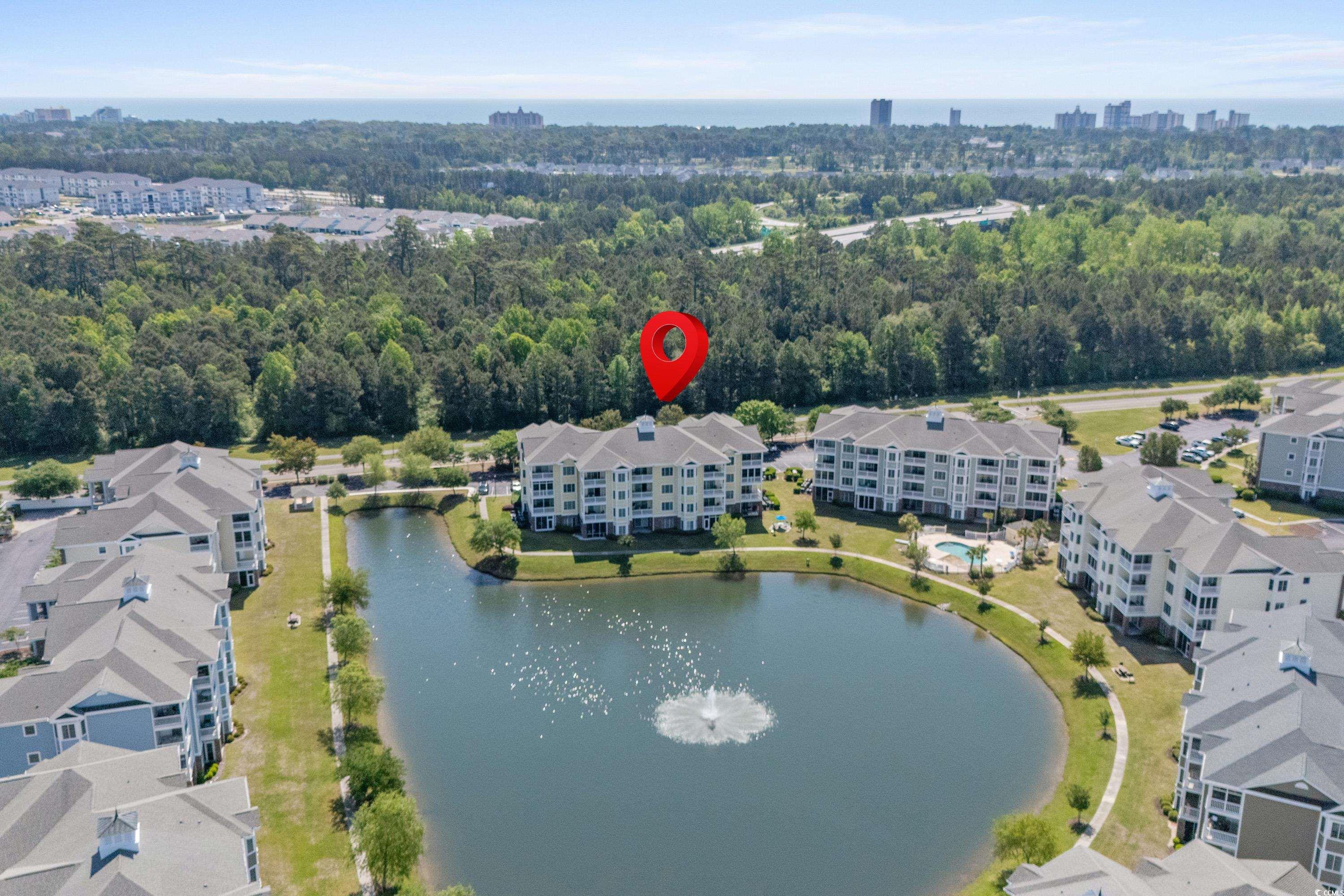 Aerial view of condominiums around a pond, with a red pin marking a building and the ocean horizon beyond.