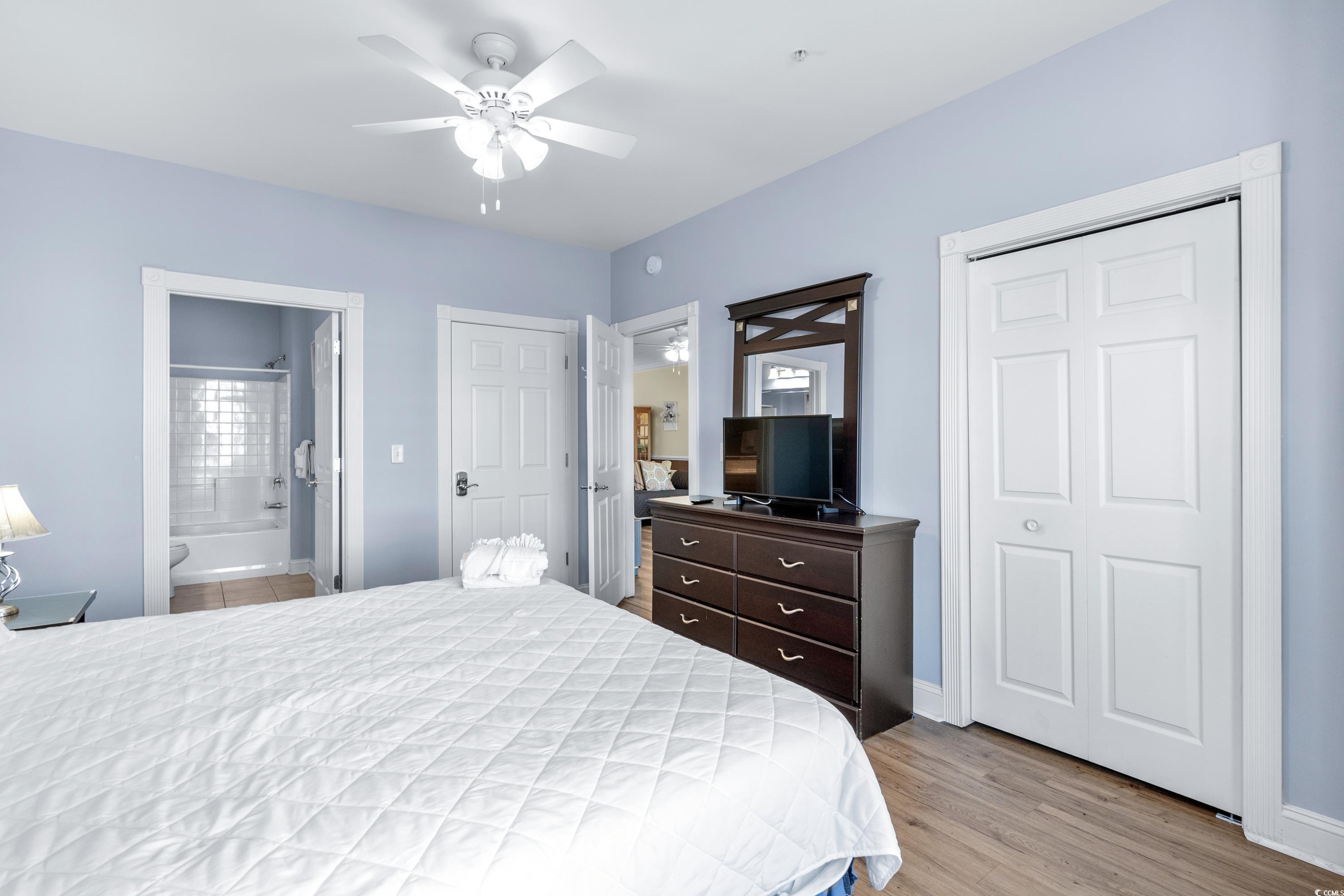 Bedroom with a white quilted bed, dark dresser and TV, double closet doors, and an open bathroom doorway.