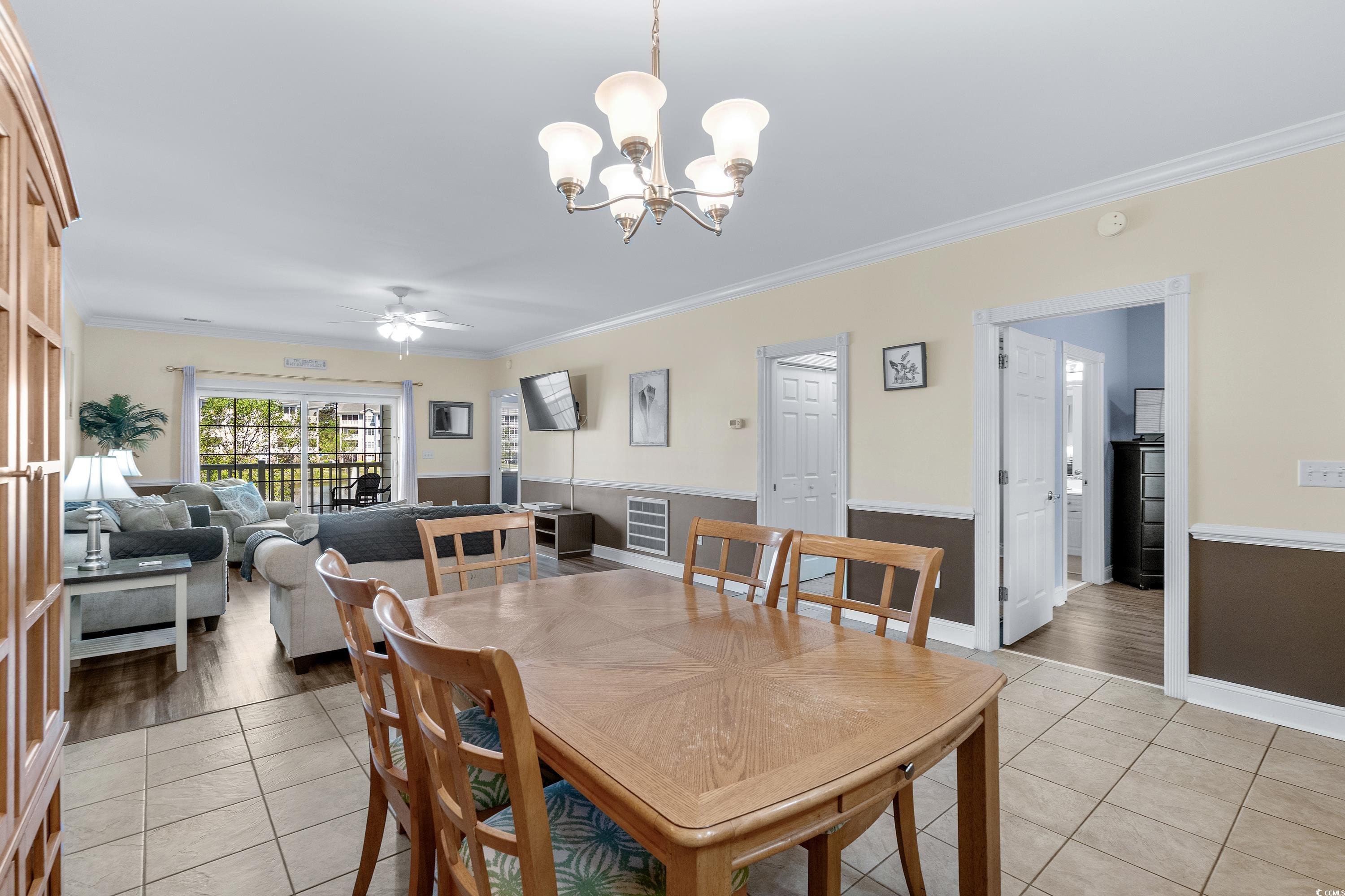 Dining area with a large wooden table overlooking a furnished living room and balcony doors.