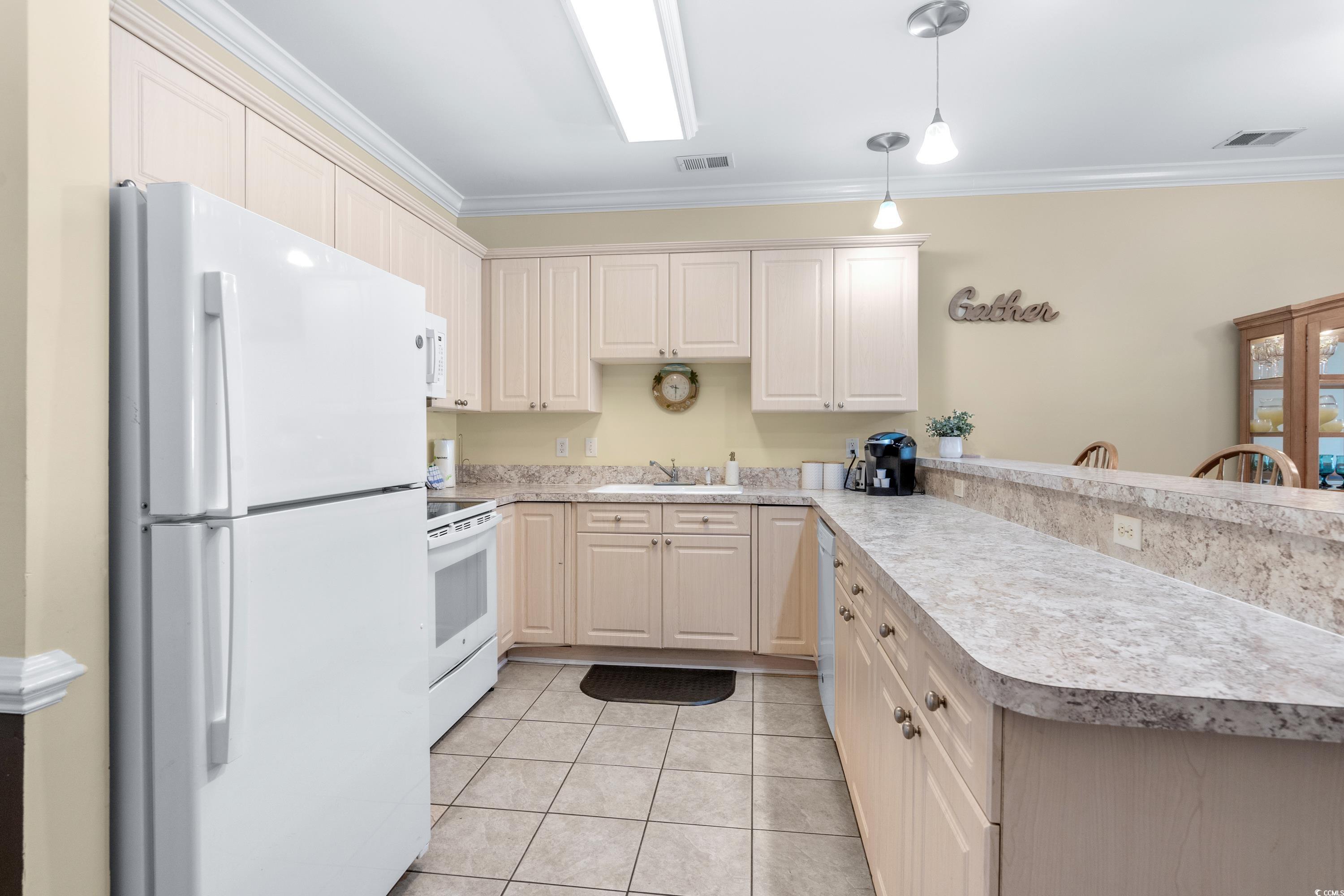 Kitchen with pale wood cabinets, white appliances, and a long stone countertop with pass-through bar.