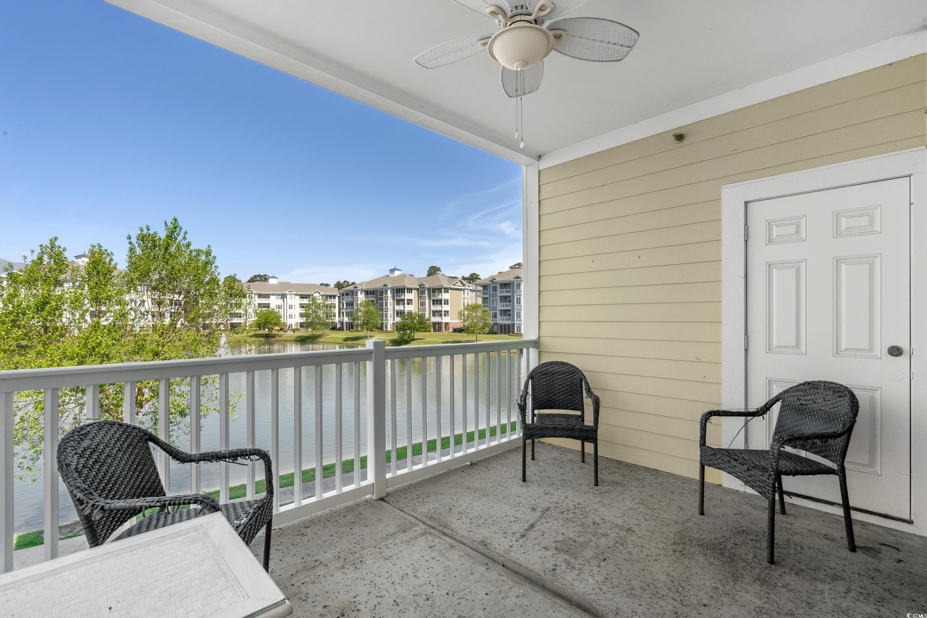 Covered balcony with wicker chairs overlooking a lake and neighboring apartment buildings.