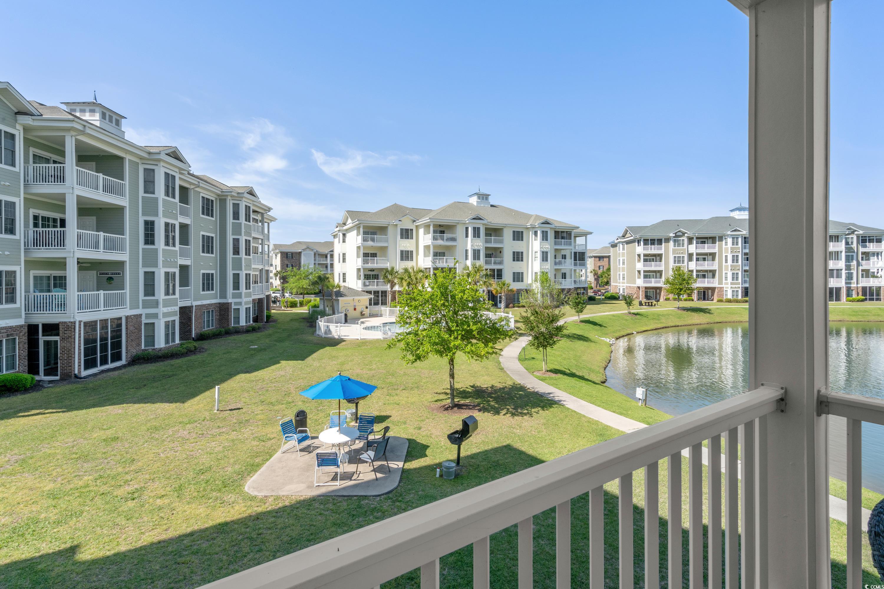 Condominium courtyard with a pond, curved path, and patio seating viewed from a balcony.