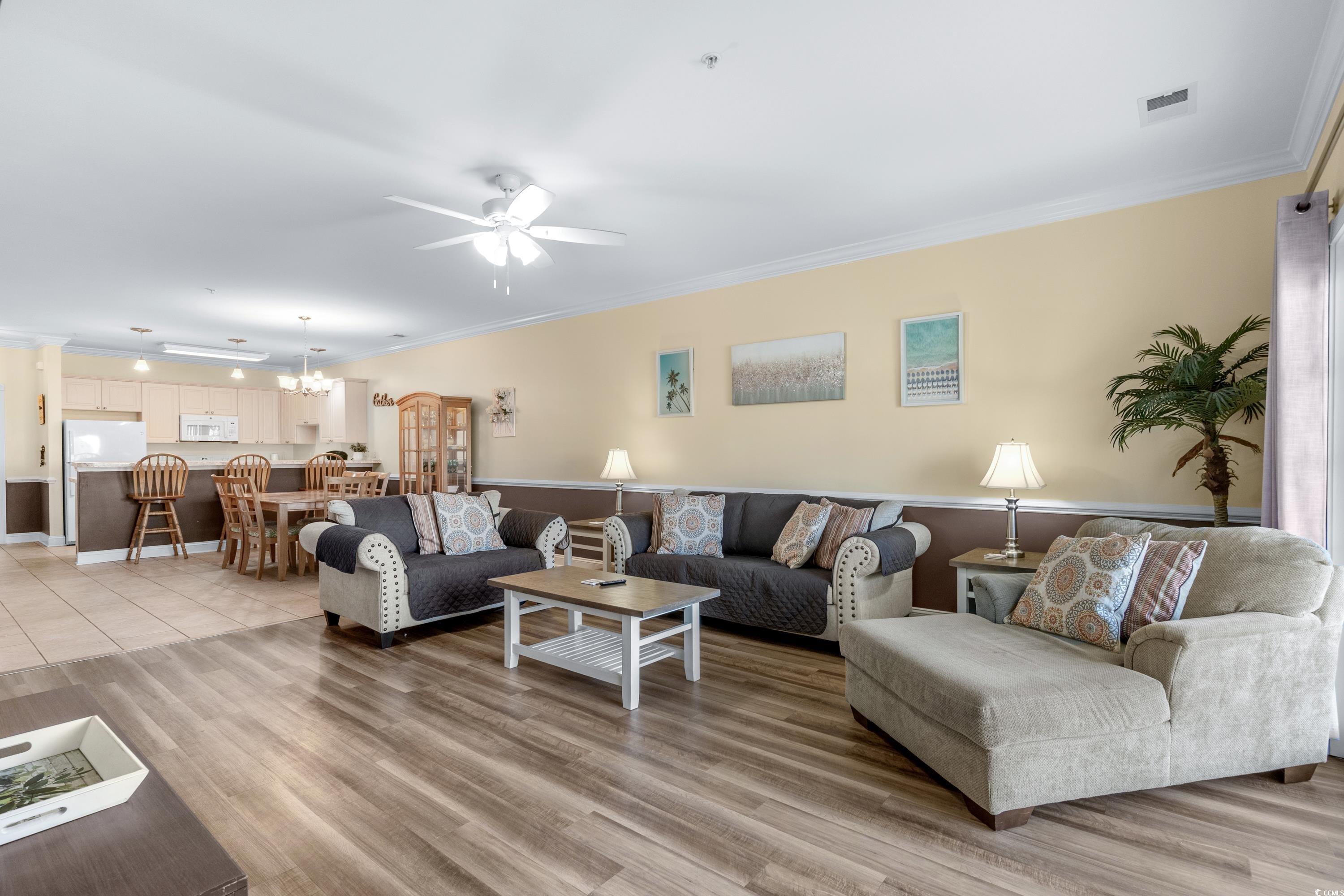Open-plan living and dining room with gray sofas, wood-look floors, and an adjoining kitchen.