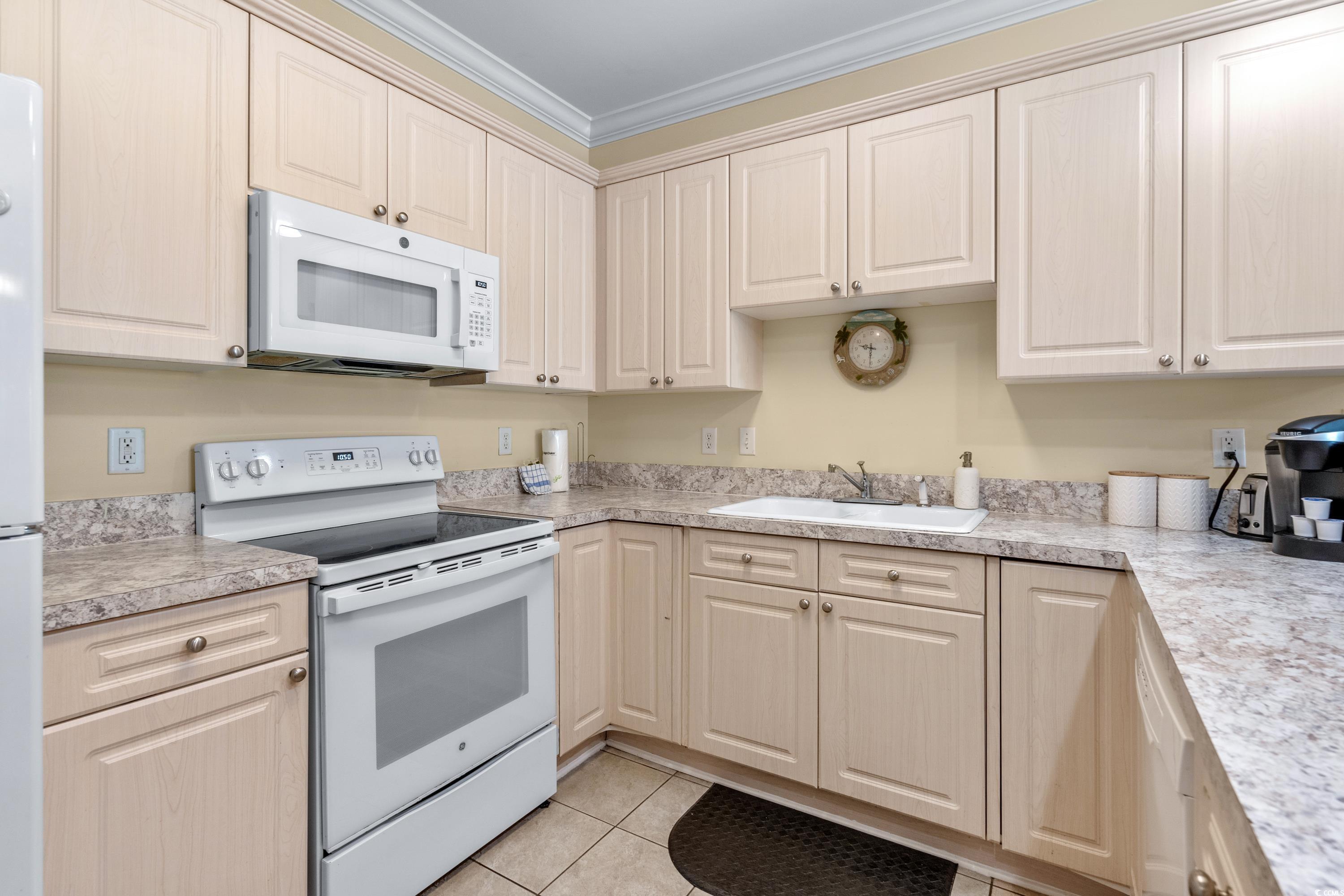 Kitchen with light wood cabinets, white range and microwave, and a sink along L-shaped countertops.