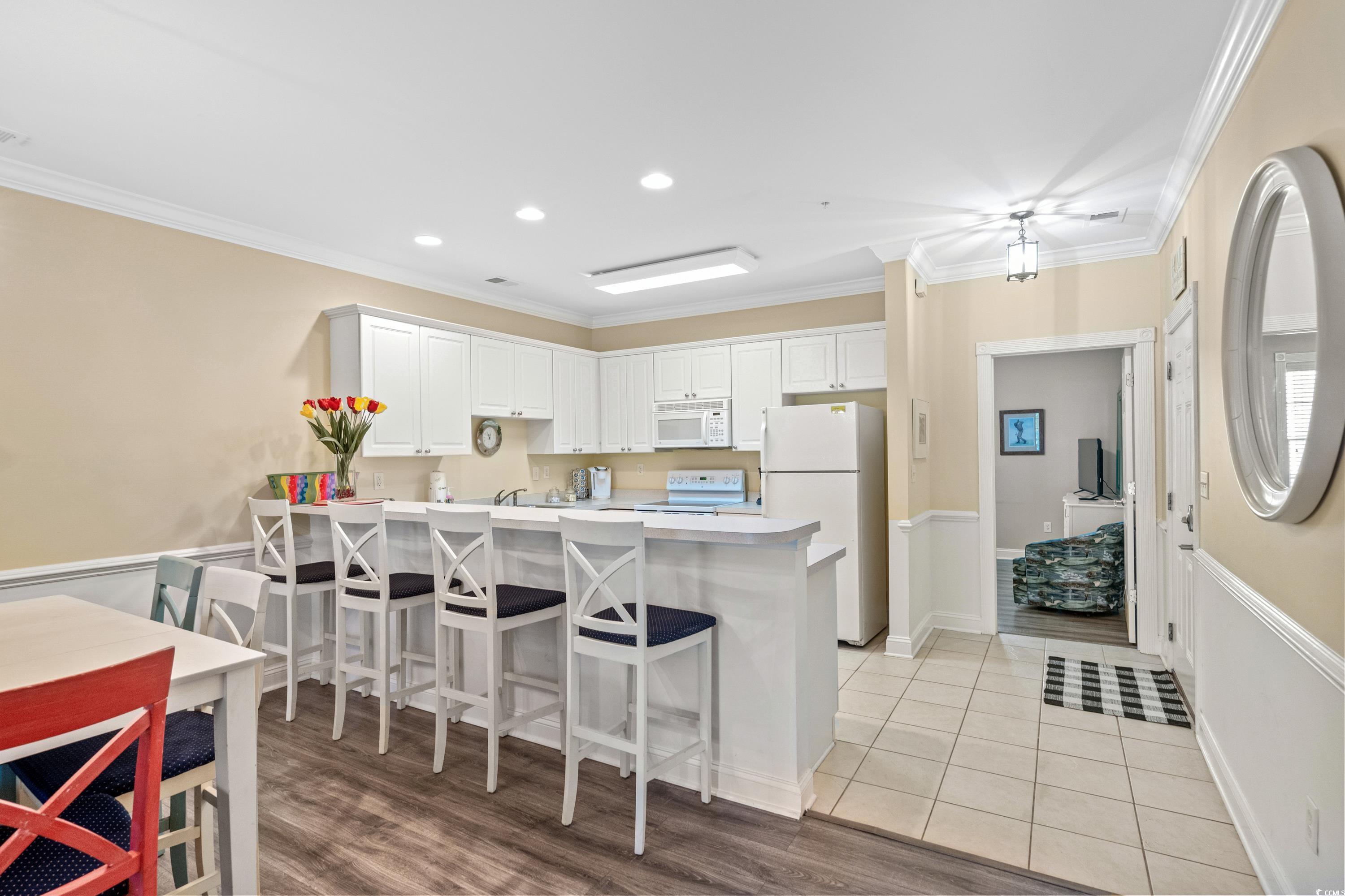 Kitchen and dining area with white cabinets, a long breakfast bar, and an adjoining sitting room.