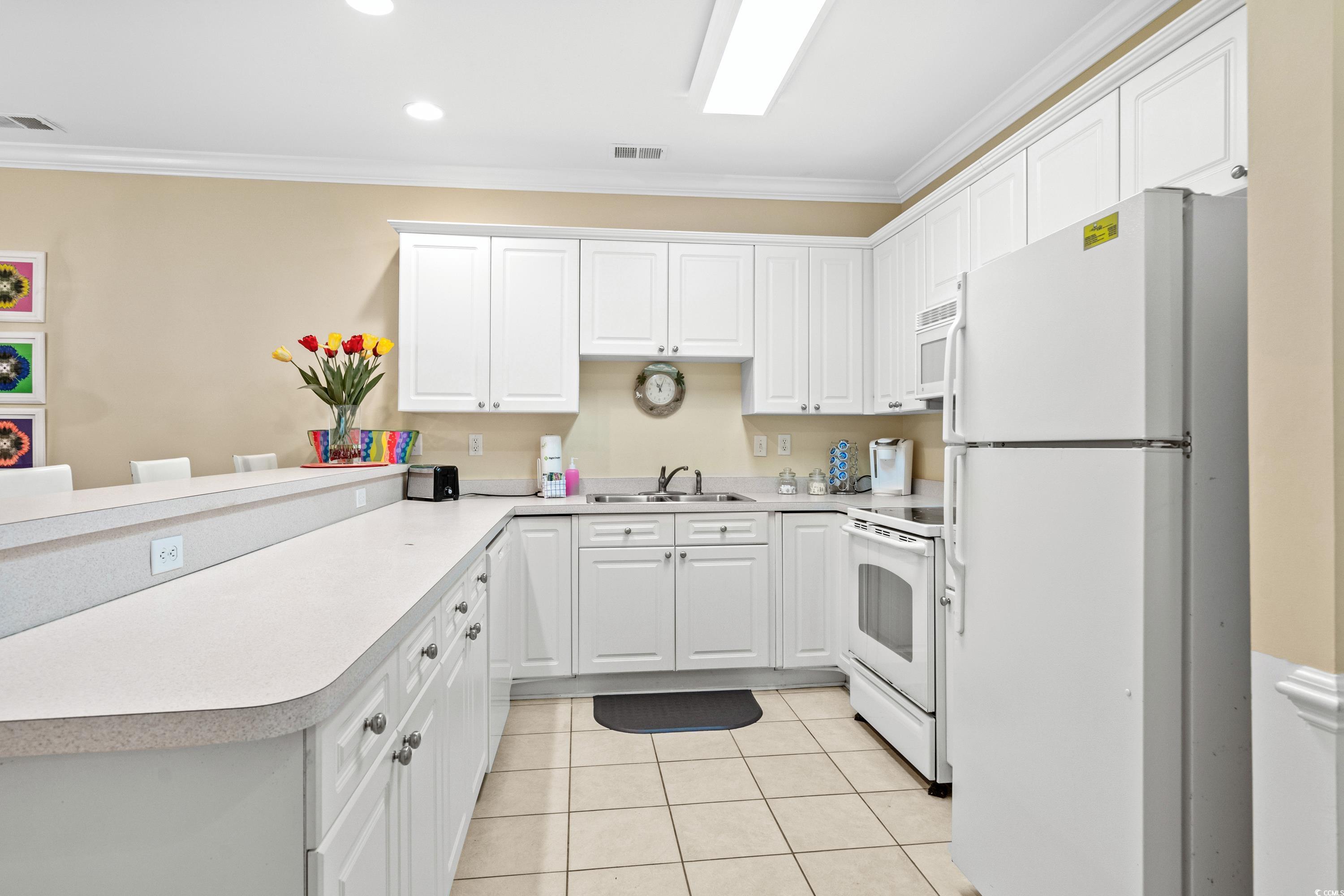 Kitchen with white cabinetry, a long peninsula, tiled floor, and colorful tulips on the counter.