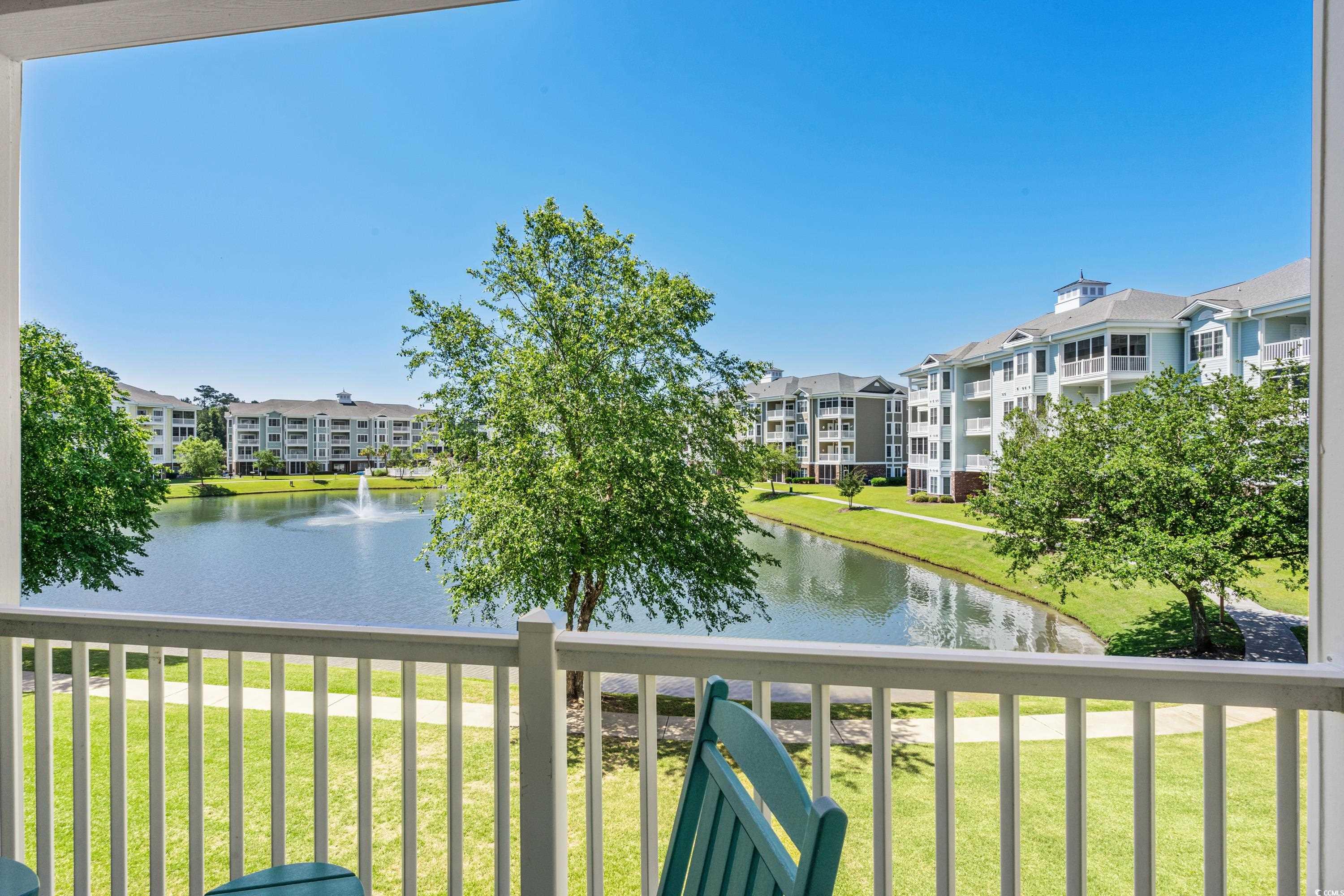 Balcony view across a landscaped pond and fountain toward multi-story residential buildings.