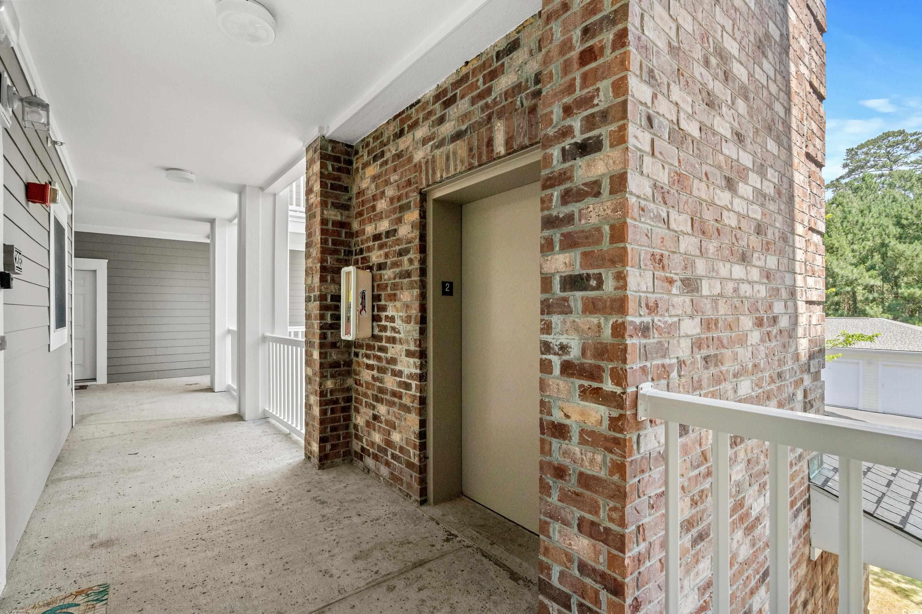 Condominium corridor with a brick elevator surround and white railing.