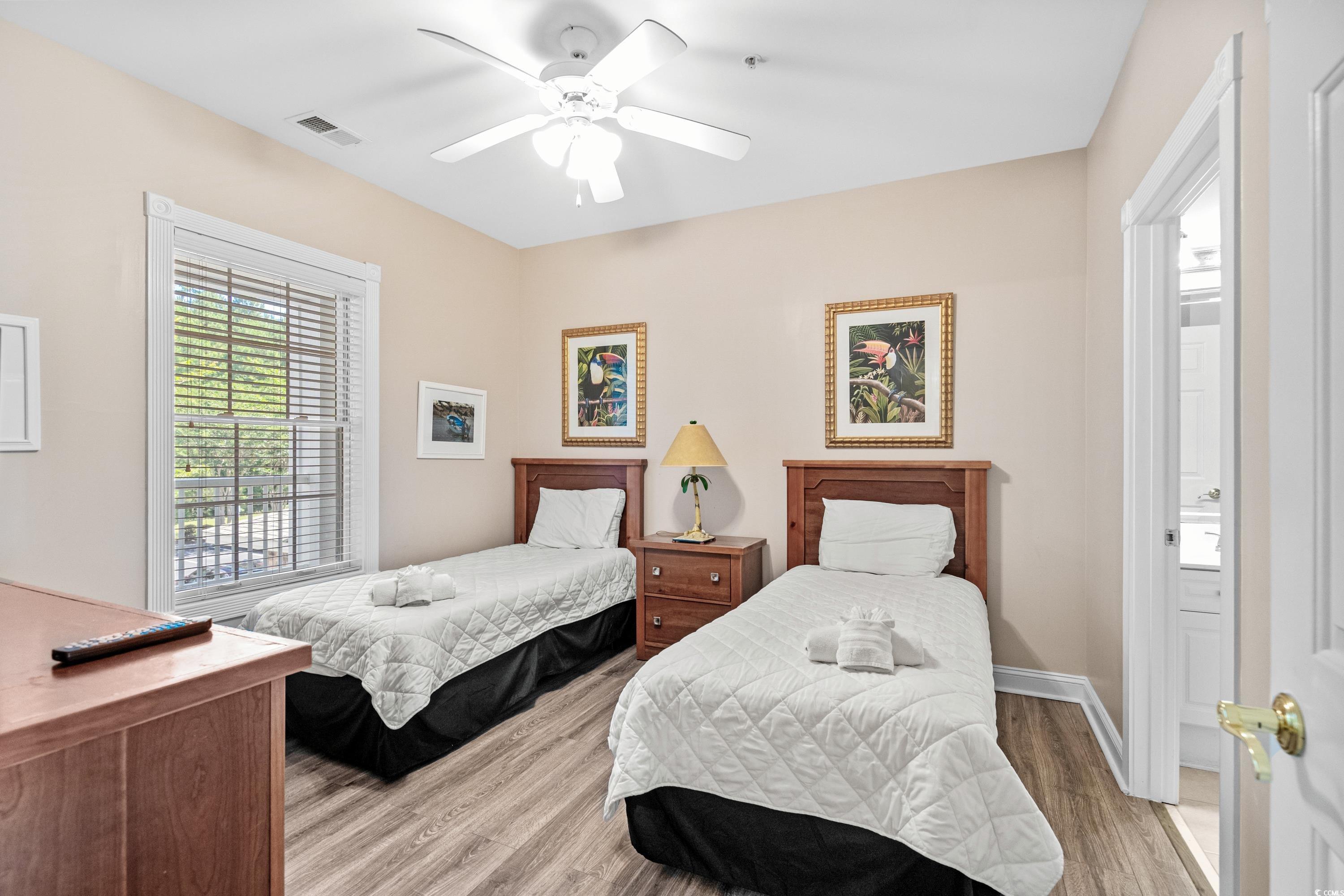 Bedroom with two twin beds, white quilts, and a large window with blinds.