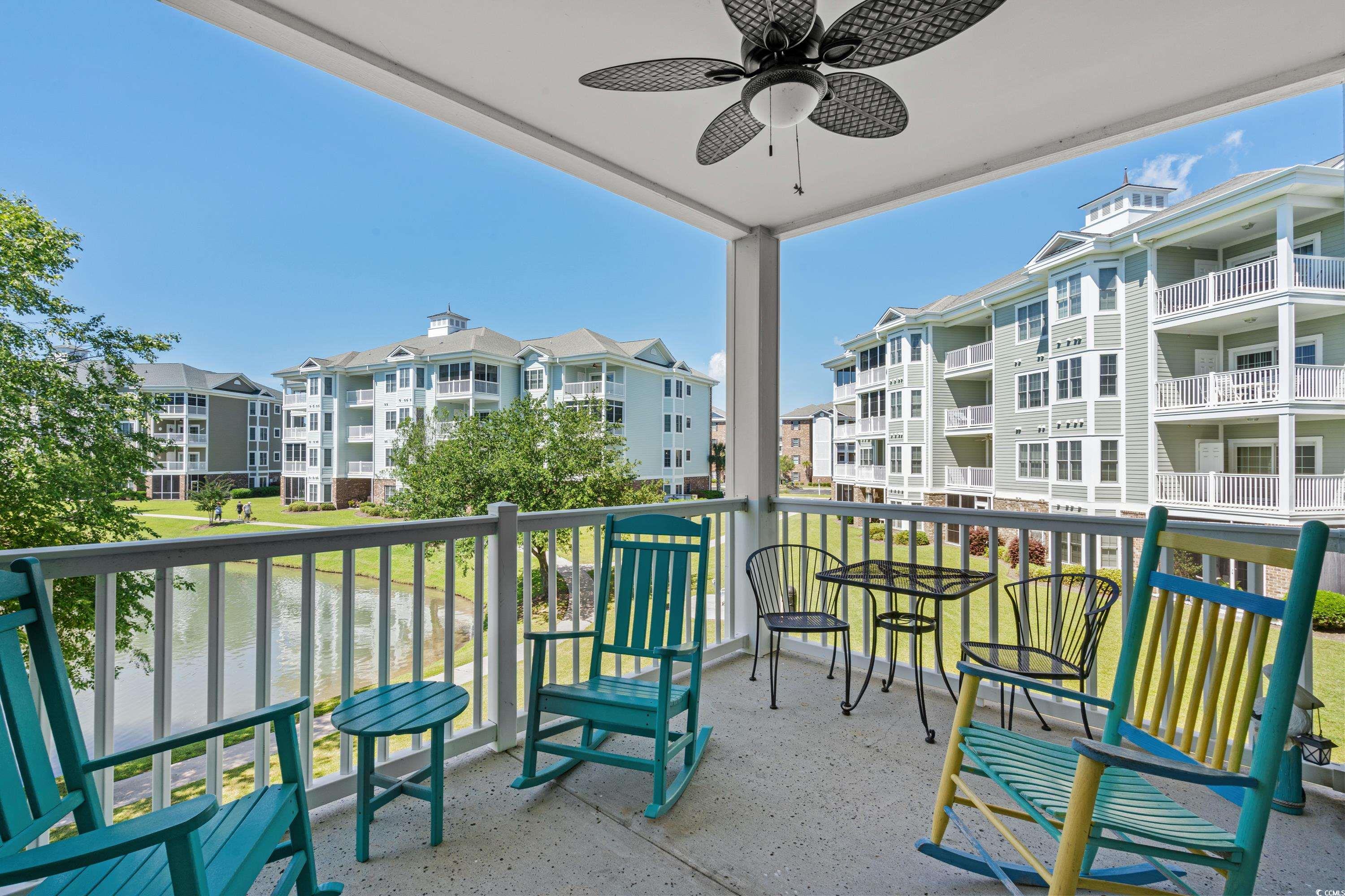 Covered balcony with colorful rocking chairs overlooking a pond and apartment buildings.