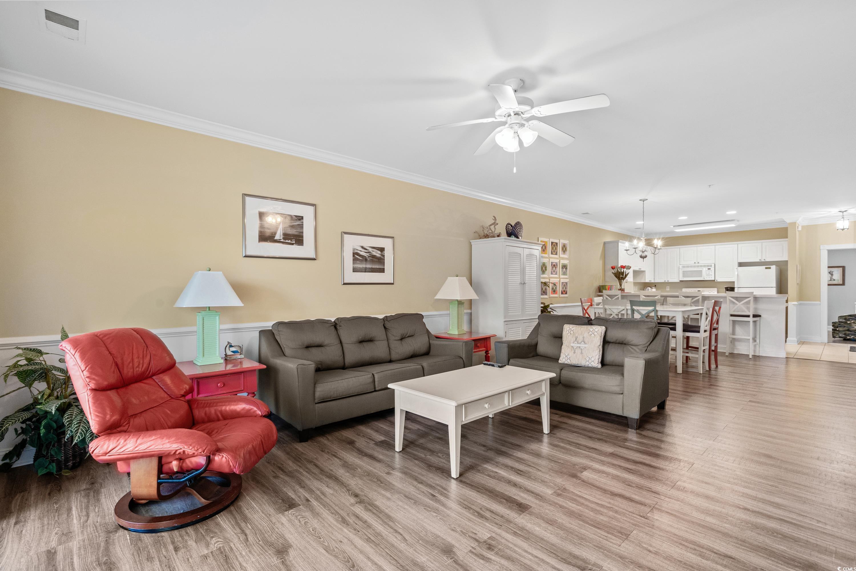 Open-plan living room with gray sofas, a red recliner, and a white kitchen beyond.